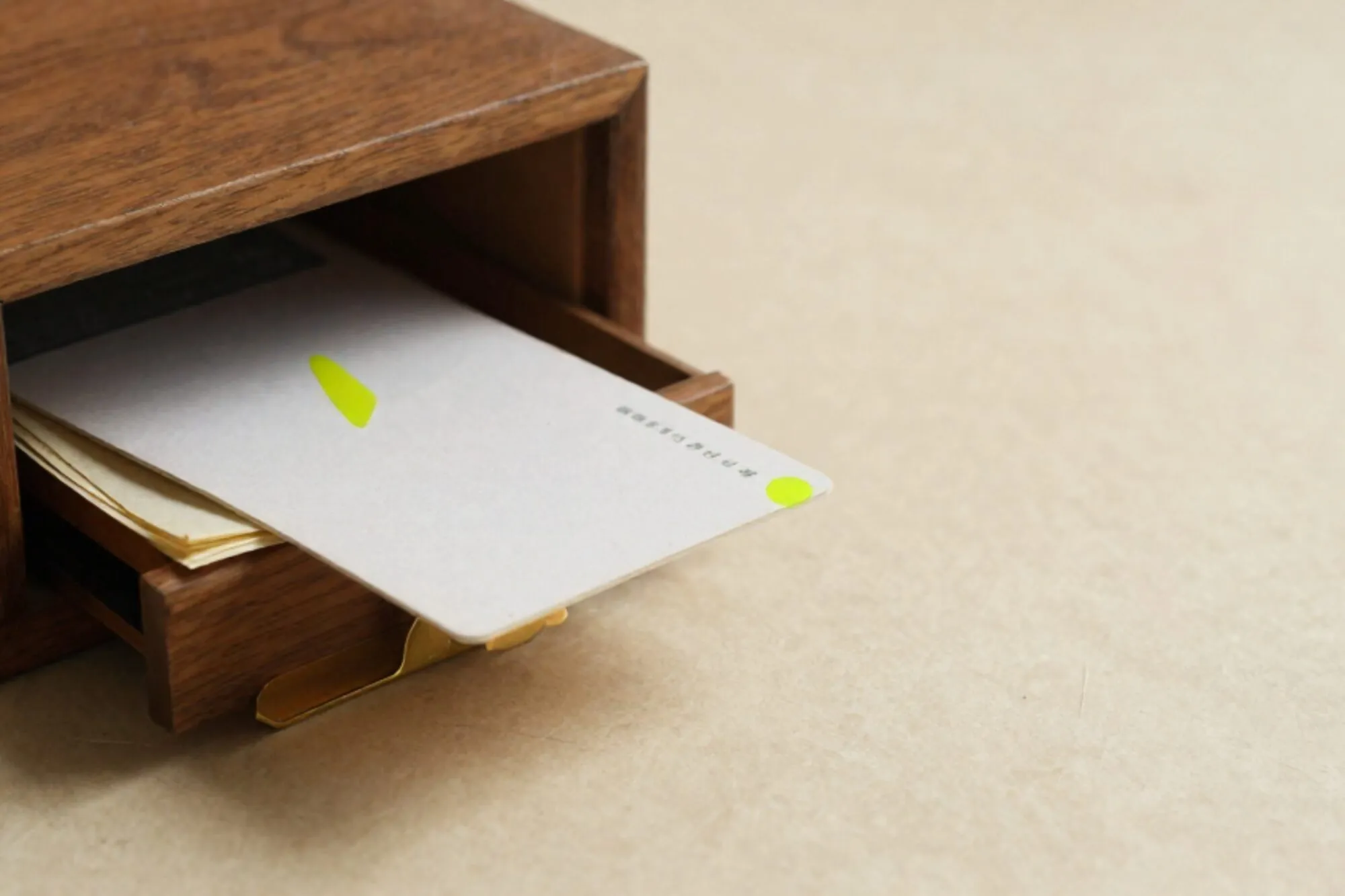 Half-open eikenhouten kaartenbak op ivoorpapier, kaart met groen tabblad, vergeelde grootboekvellen en messing scheider ernaast.