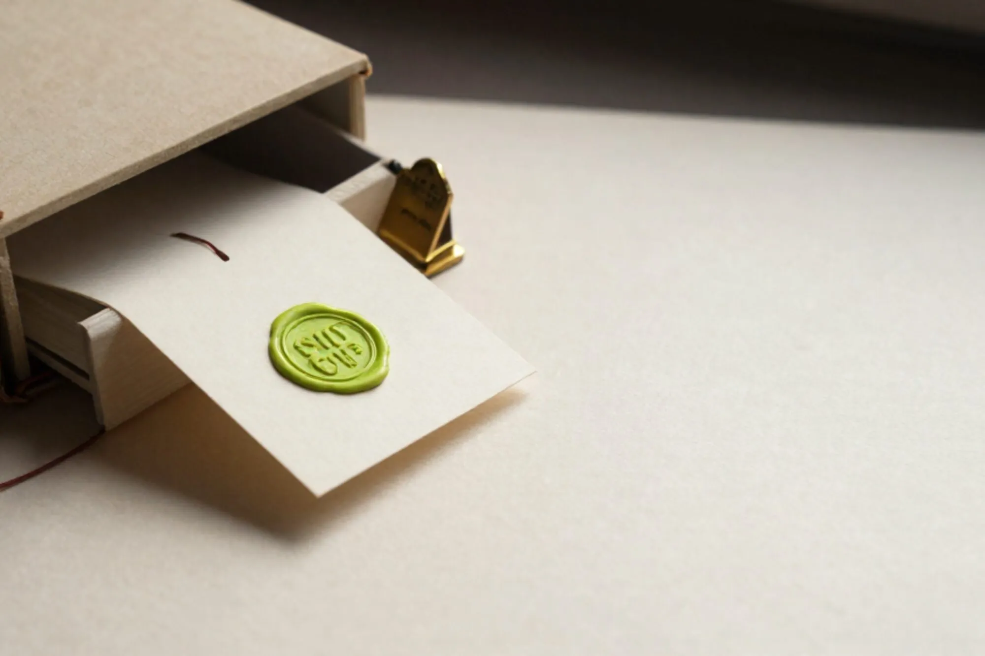 Open index-card drawer with brass divider and cream card sealed in chartreuse wax on ivory linen, leather ledger at left.