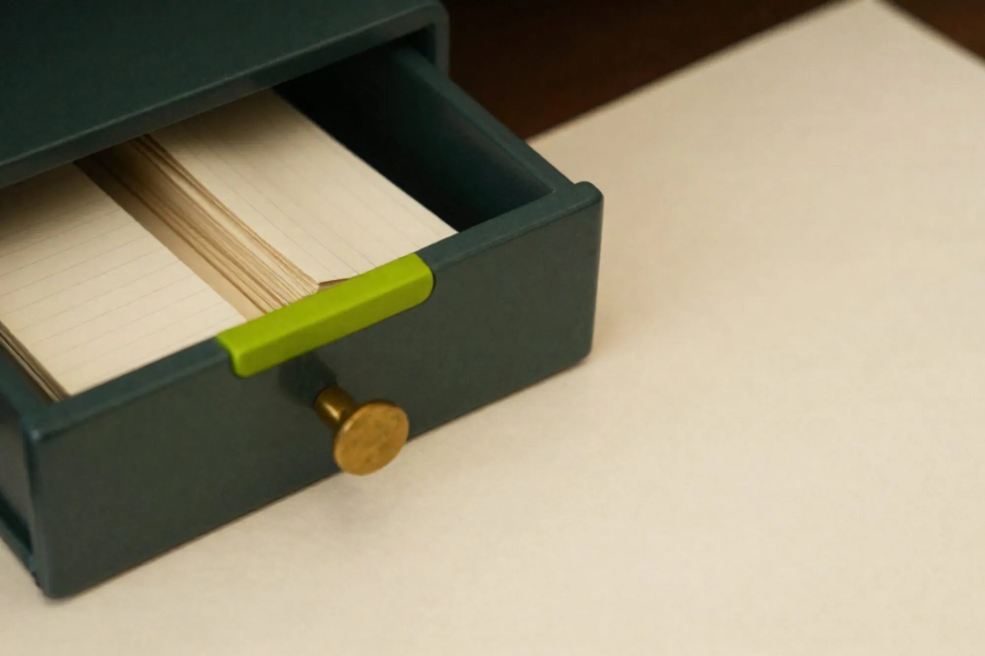 Open eiken kaartenbaklade met groene tab, drie stapels crème papier en messing strip op ivoorkleurig oppervlak.