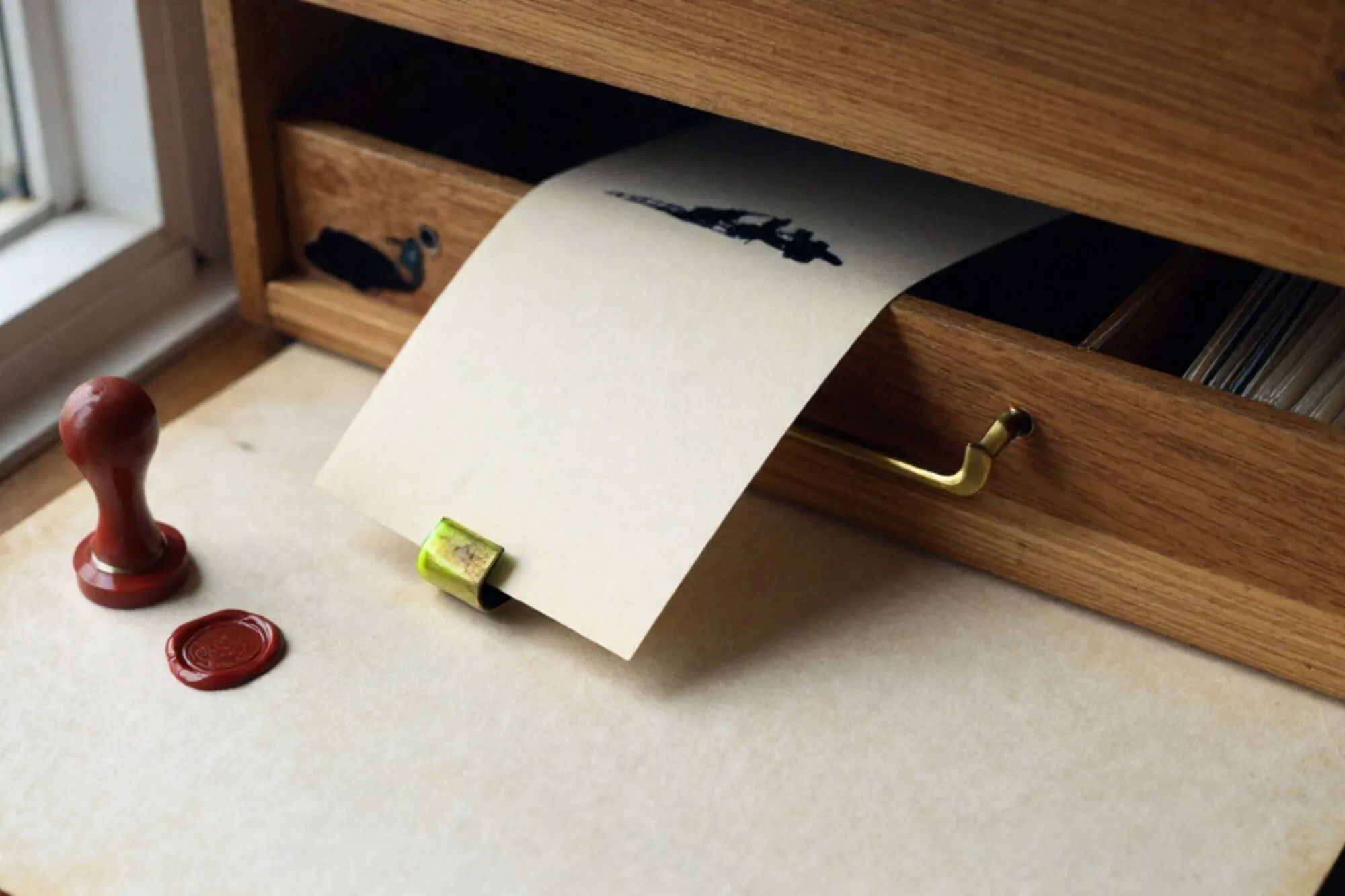 Open eiken kaartenbaklade op linnen, één crème kaart omhoog met groen lint, messing tussenschot, rode lakzegel op briefje.