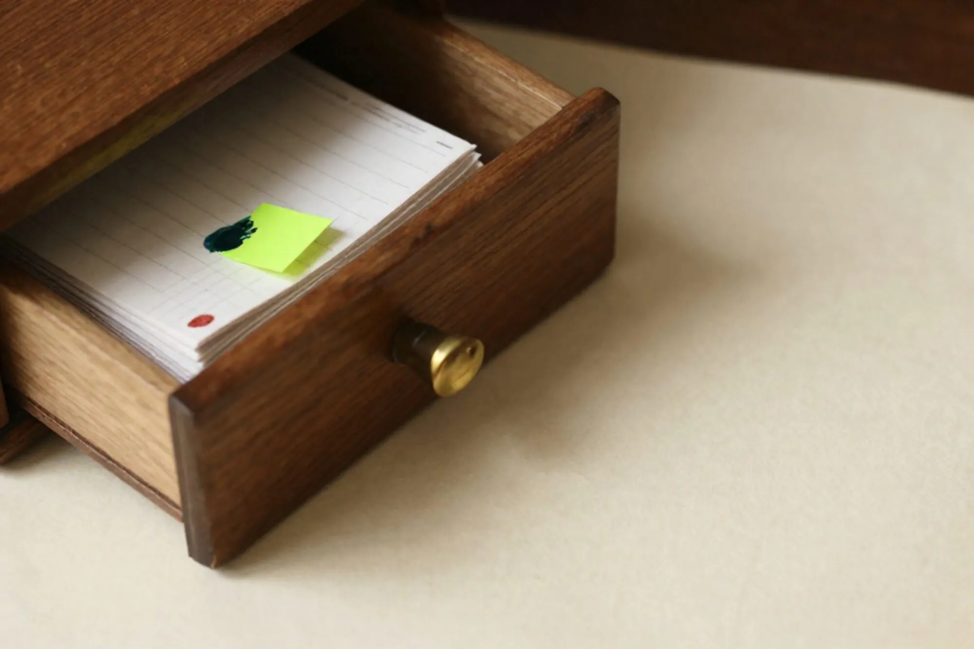 Open wooden index-card drawer with ledger paper, brass divider, green tab, red wax seal on ivory desk.
