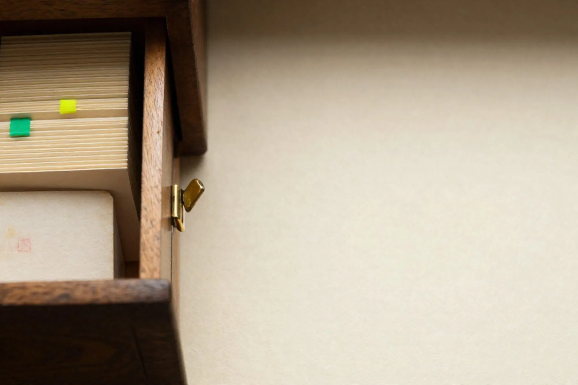 Half-open oak index-card drawer with cream cards, one chartreuse tab, brass divider, stamped card on ivory paper.