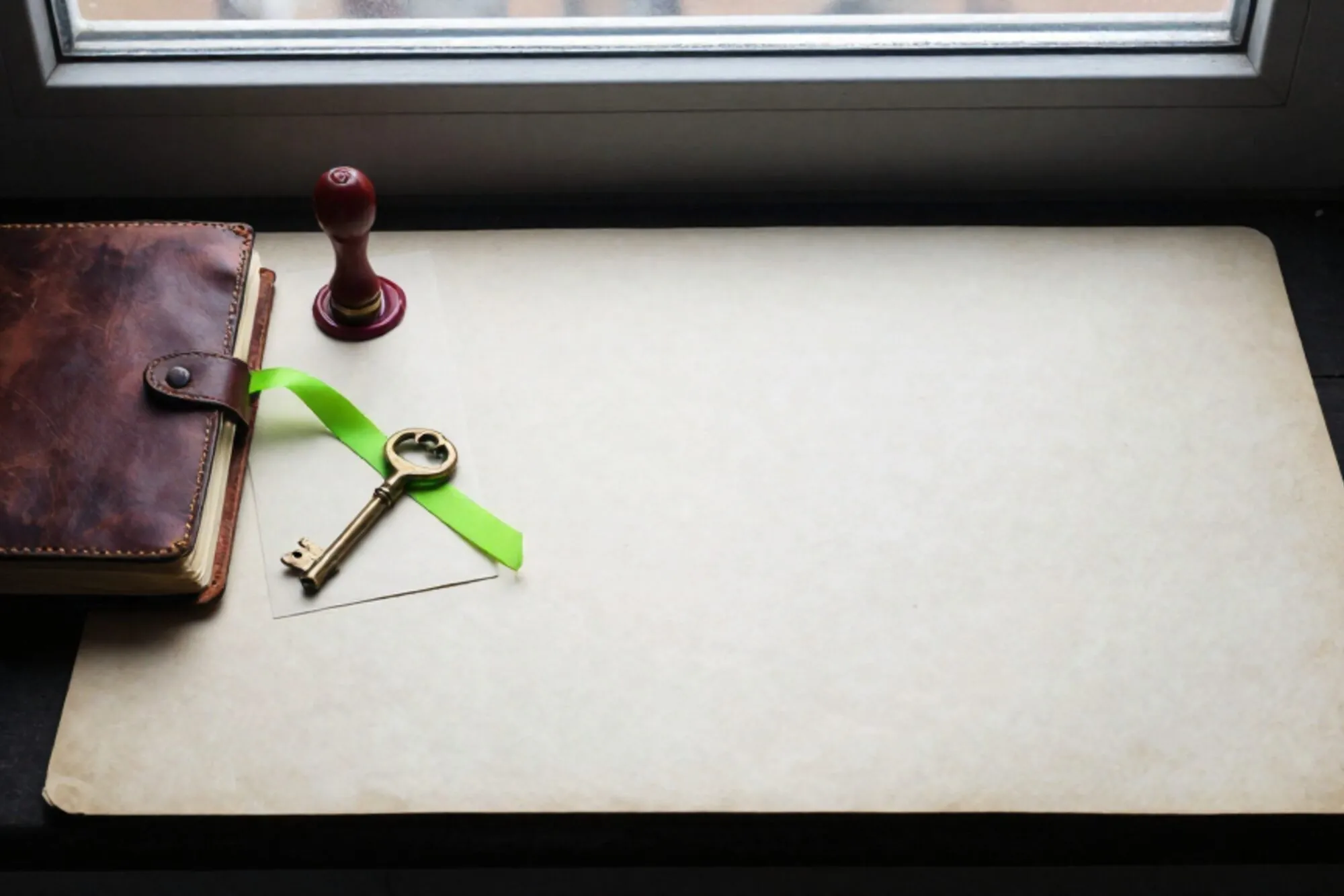 Open leather logbook, brass key on cream card, green ribbon between pages, red wax seal on ivory paper.
