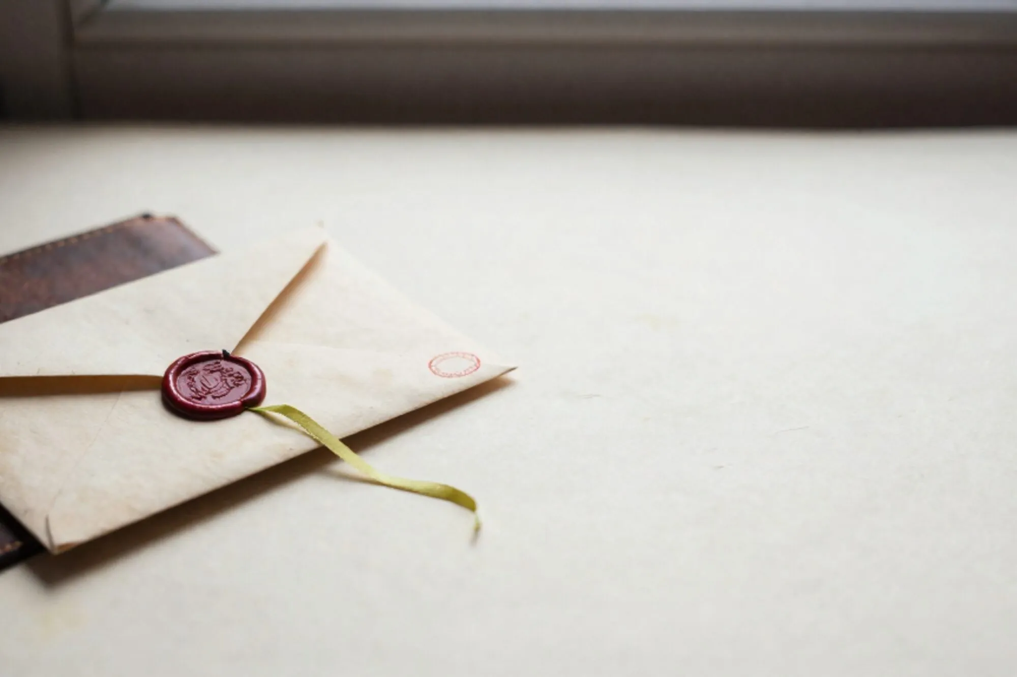 Versleten manilla envelop met gebarsten donkergroen lakzegel, groen lint, rode stempel op ivoor papier.