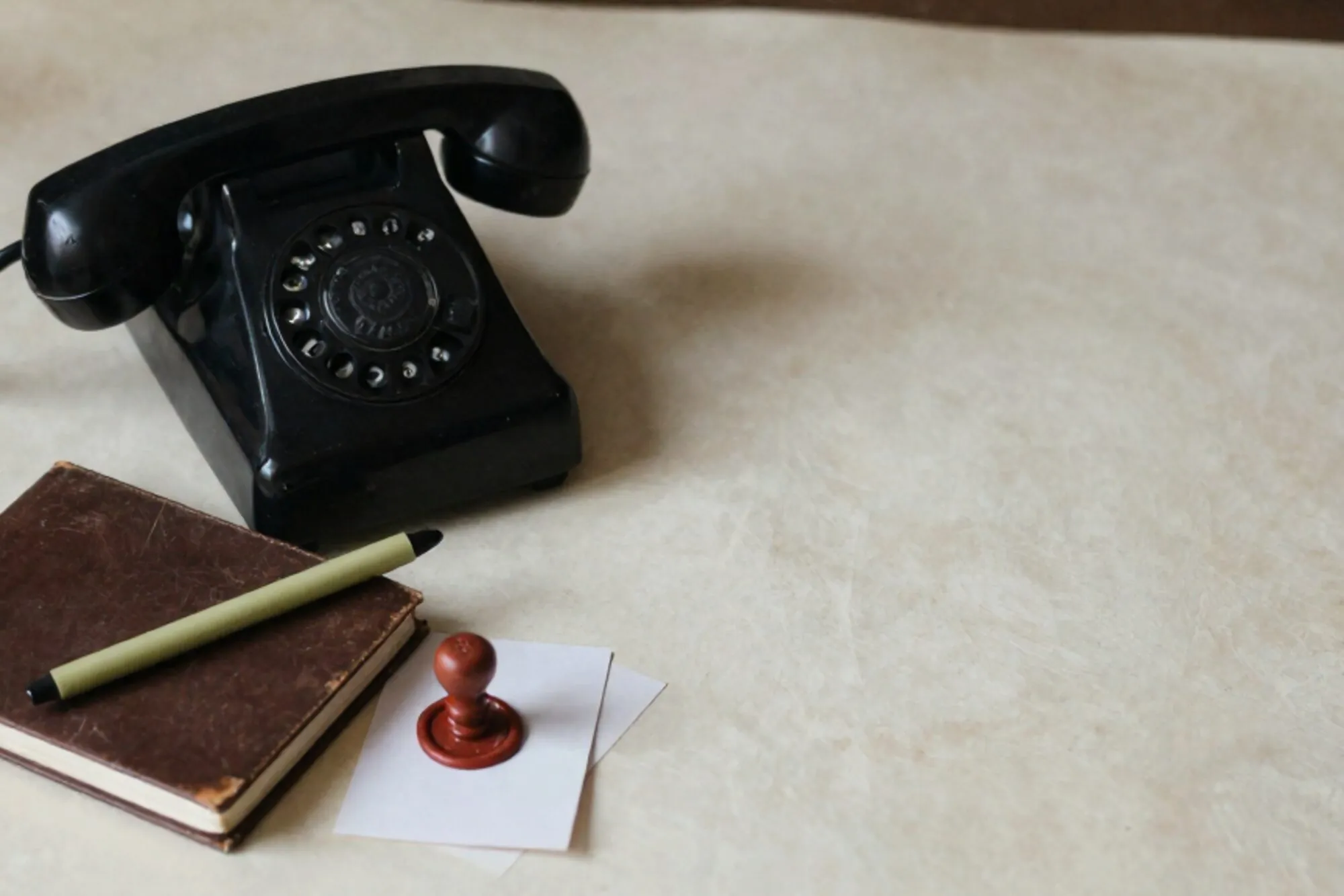 Zwarte bakelieten telefoonhoorn op leren onderlegger, groen lint op bruin notitieboek, rode lakzegel op kaart.