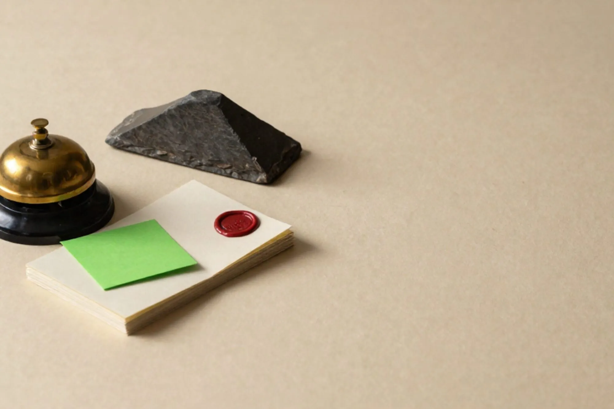 Brass hotel call-bell on ivory paper beside cream dockets, a chartreuse index card, slate tile, red wax seal.