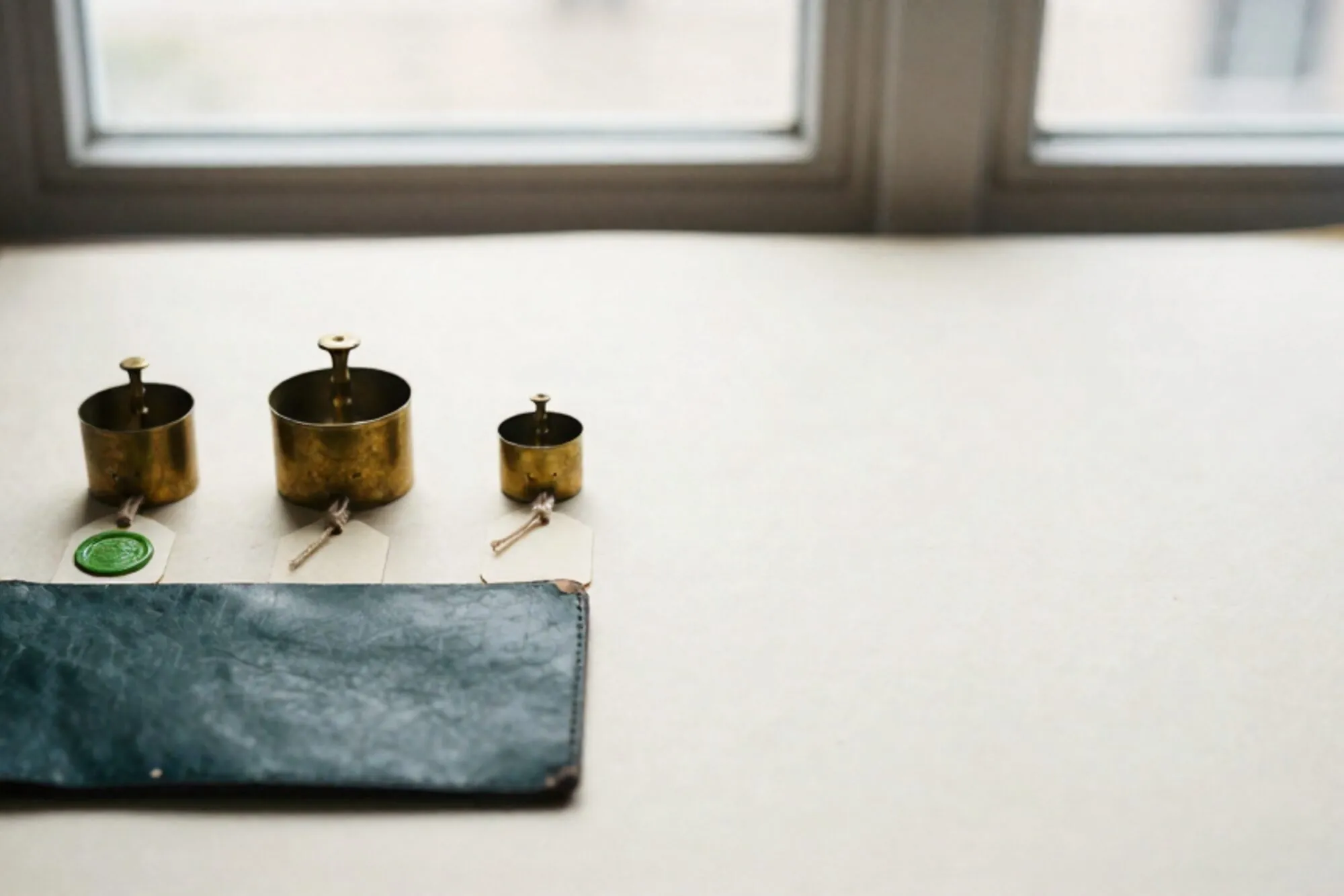 Three antique brass weights on cream paper tags with linen thread, one green wax seal, on ivory paper surface.