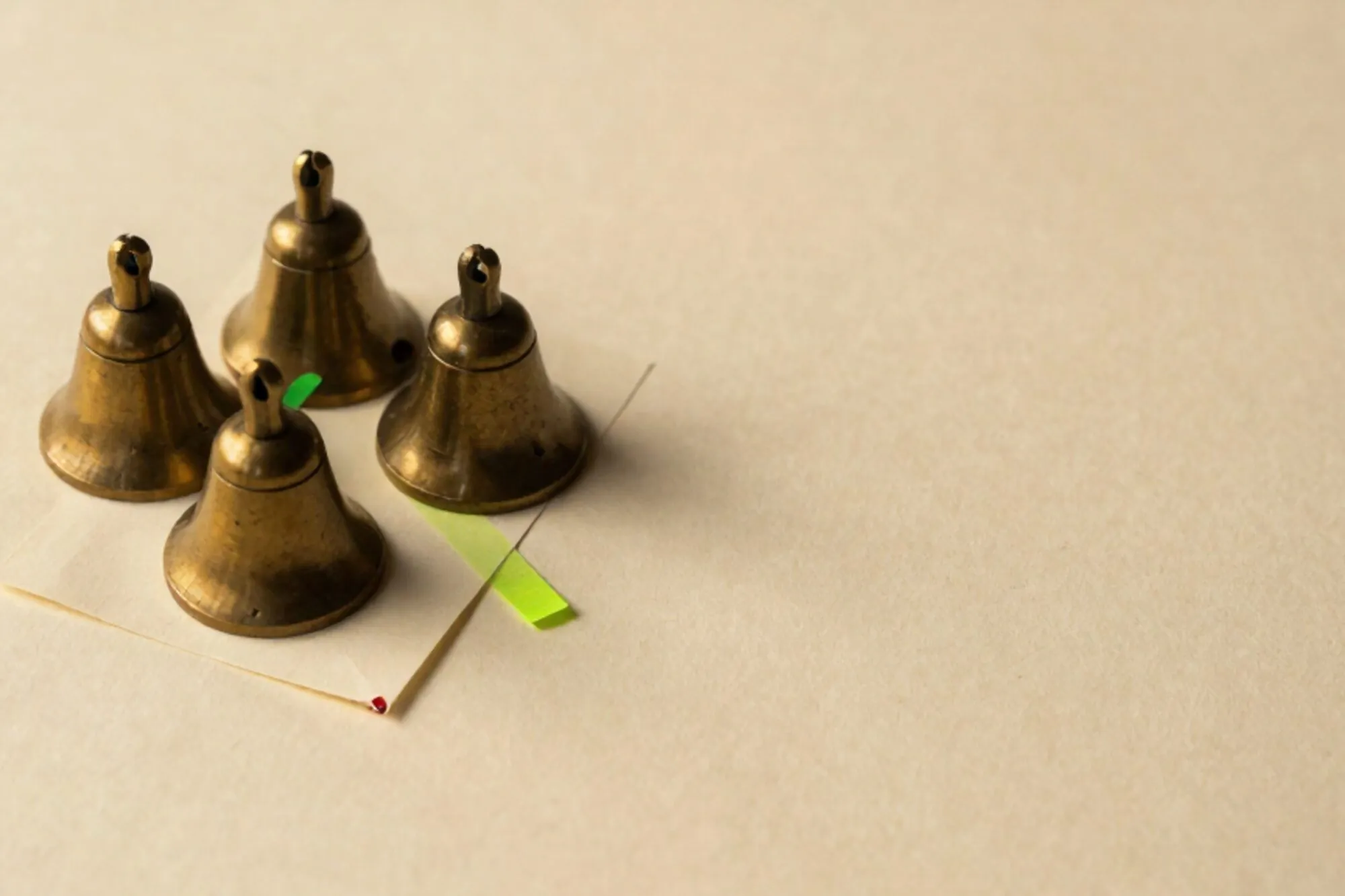 Three brass desk bells clustered on ivory paper beside a folded cream NDA with green ribbon and red wax seal.