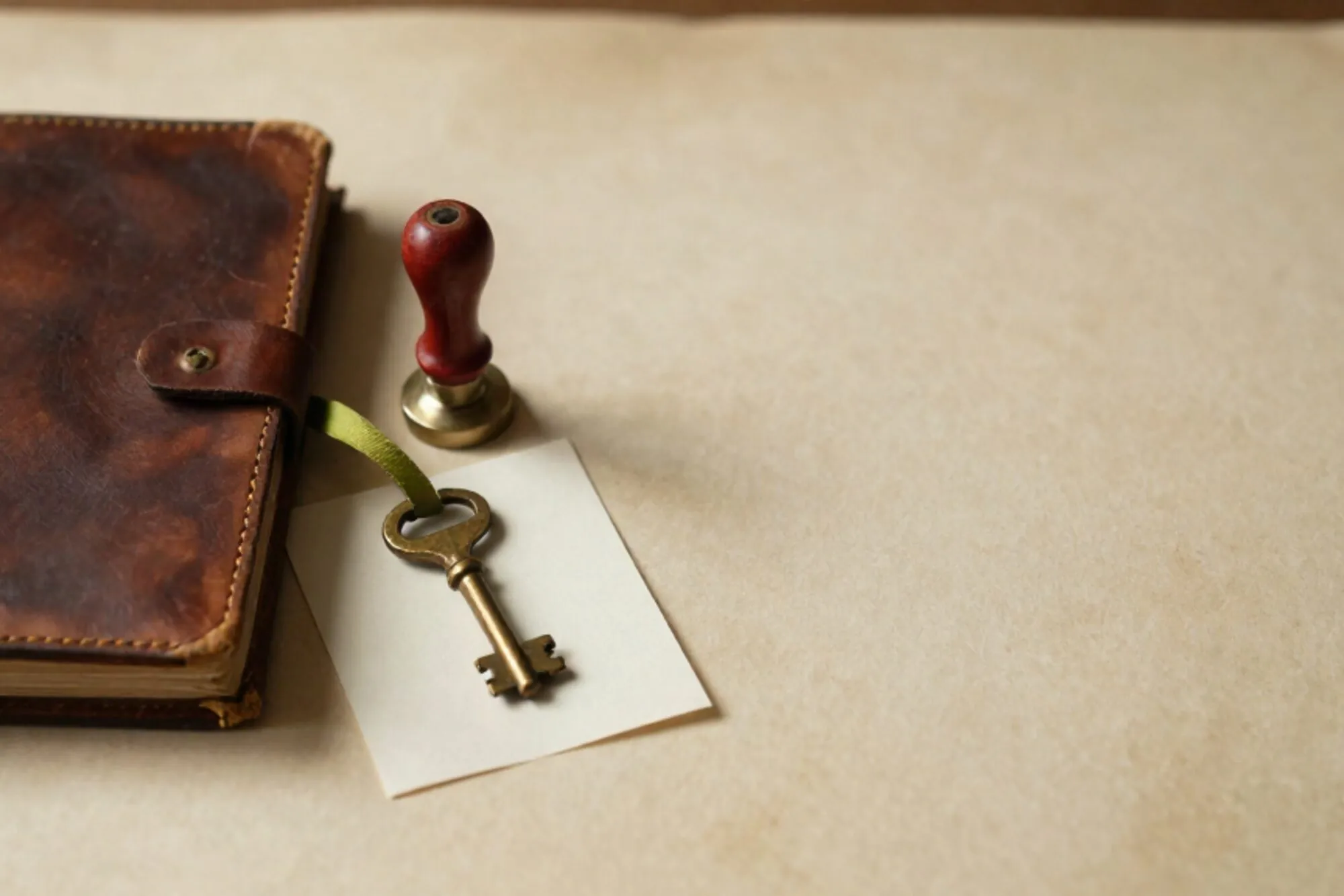Closed leather logbook, brass key on cream card with green ribbon, red wax seal on ivory paper, side light.
