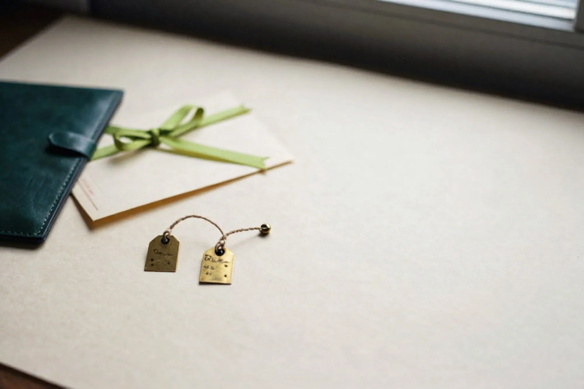 Two brass postal tags linked by waxed thread beside a folded cream telegram with green ribbon on an ivory desk.