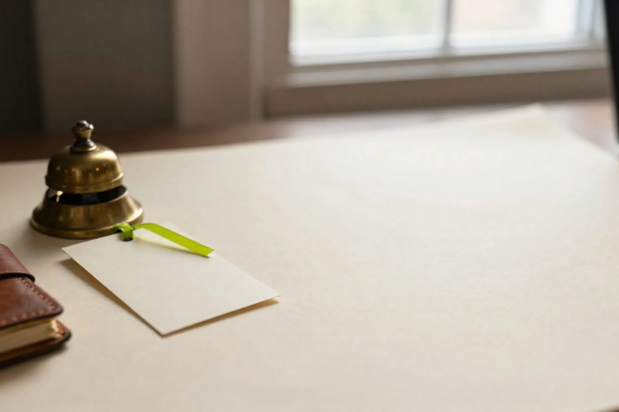 Koperen bel, crème indexkaart met groen lint, leren agenda met rode bladwijzer op ivoren bureau.