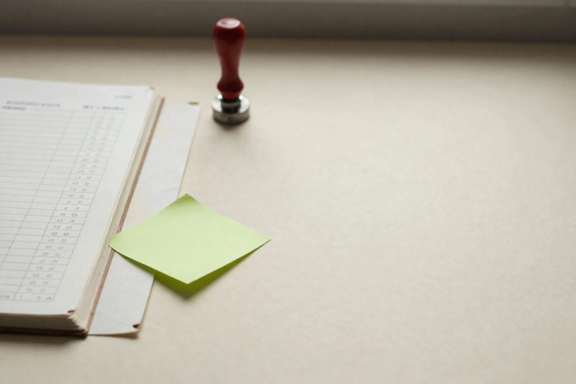 Open craft-paper ledger on ivory desk, torn page with product card rows, green sticky tag, broken red wax seal.