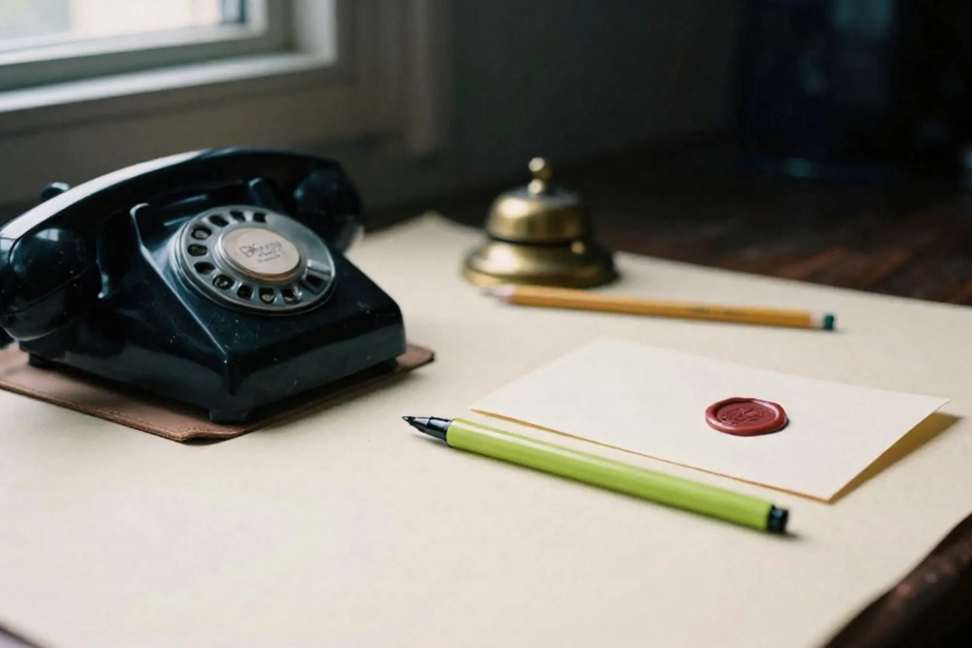 Black bakelite desk phone receiver off-hook on leather blotter, green silk ribbon across cradle, wax-sealed card beside.