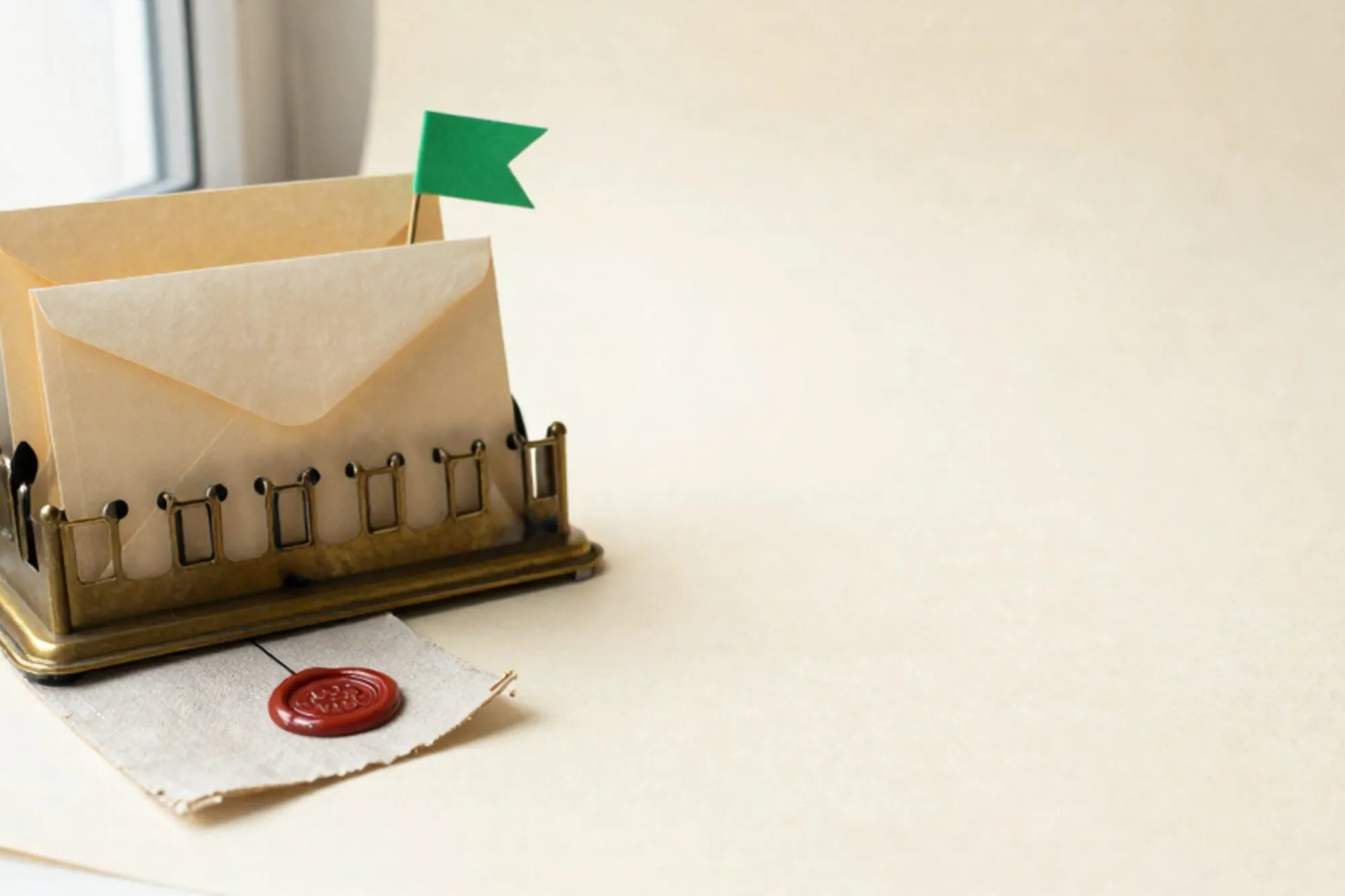 Brass letter-sorting rack with three cream envelopes, one with green flag, red wax seal on linen, ivory paper.