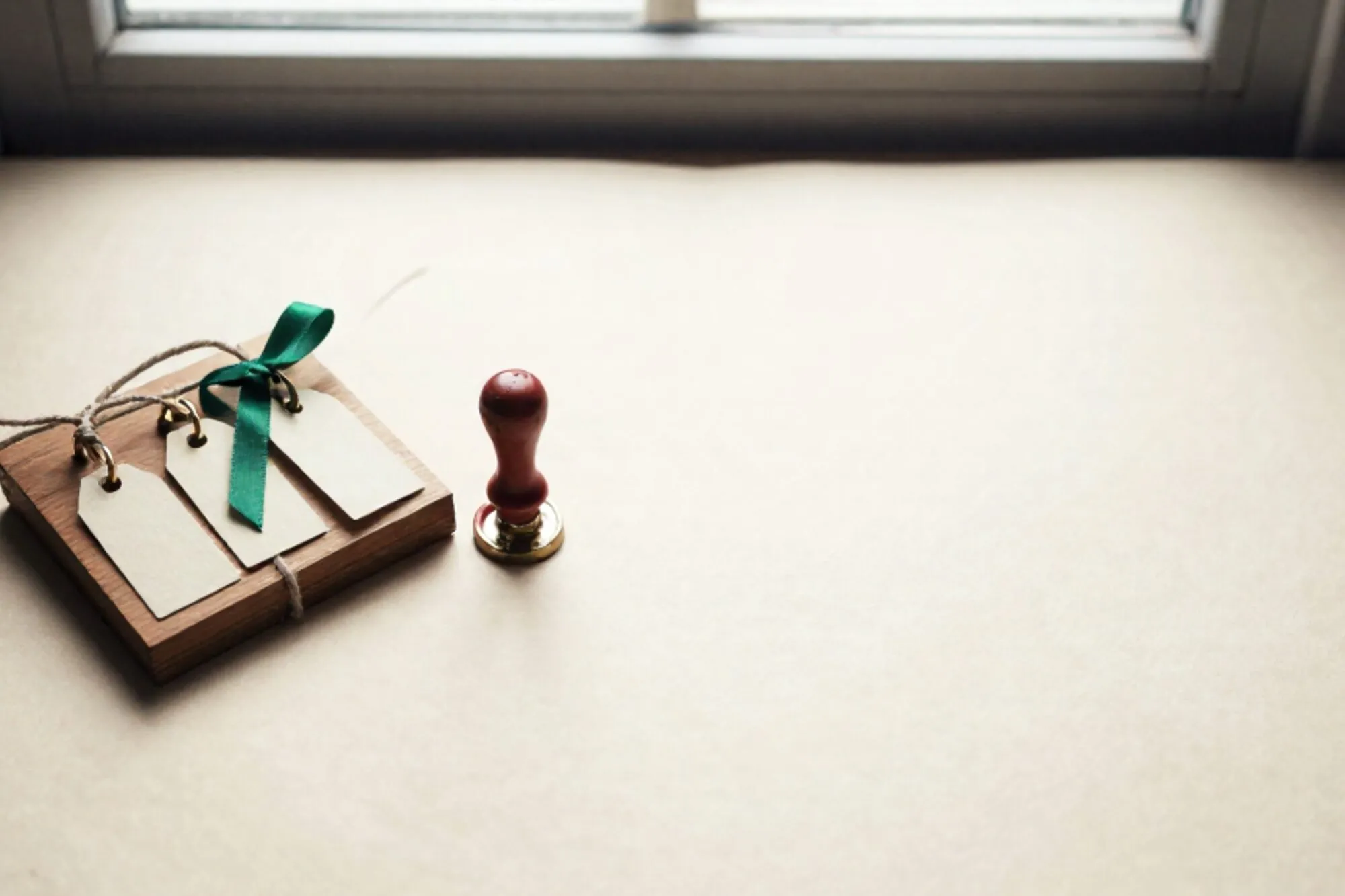Houten sorteerbord met drie messing labels aan touw, één groen lint, rode lakzegel op crème vrachtbrief, ivoren tafel.