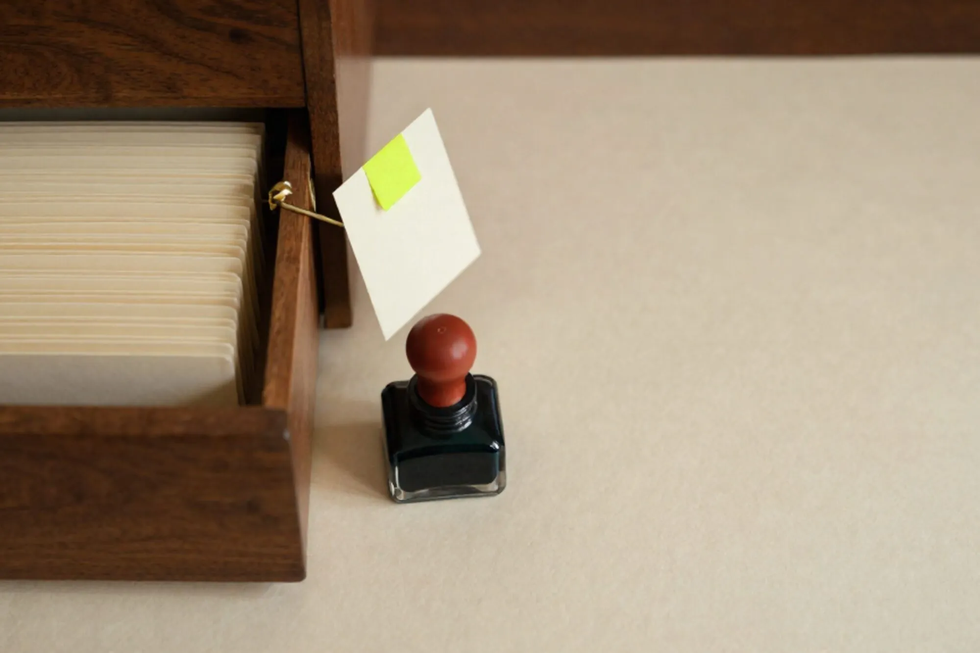 Open wooden index-card drawer with cream cards, one lifted card with green tab and brass divider, red wax seal on ink blotter.