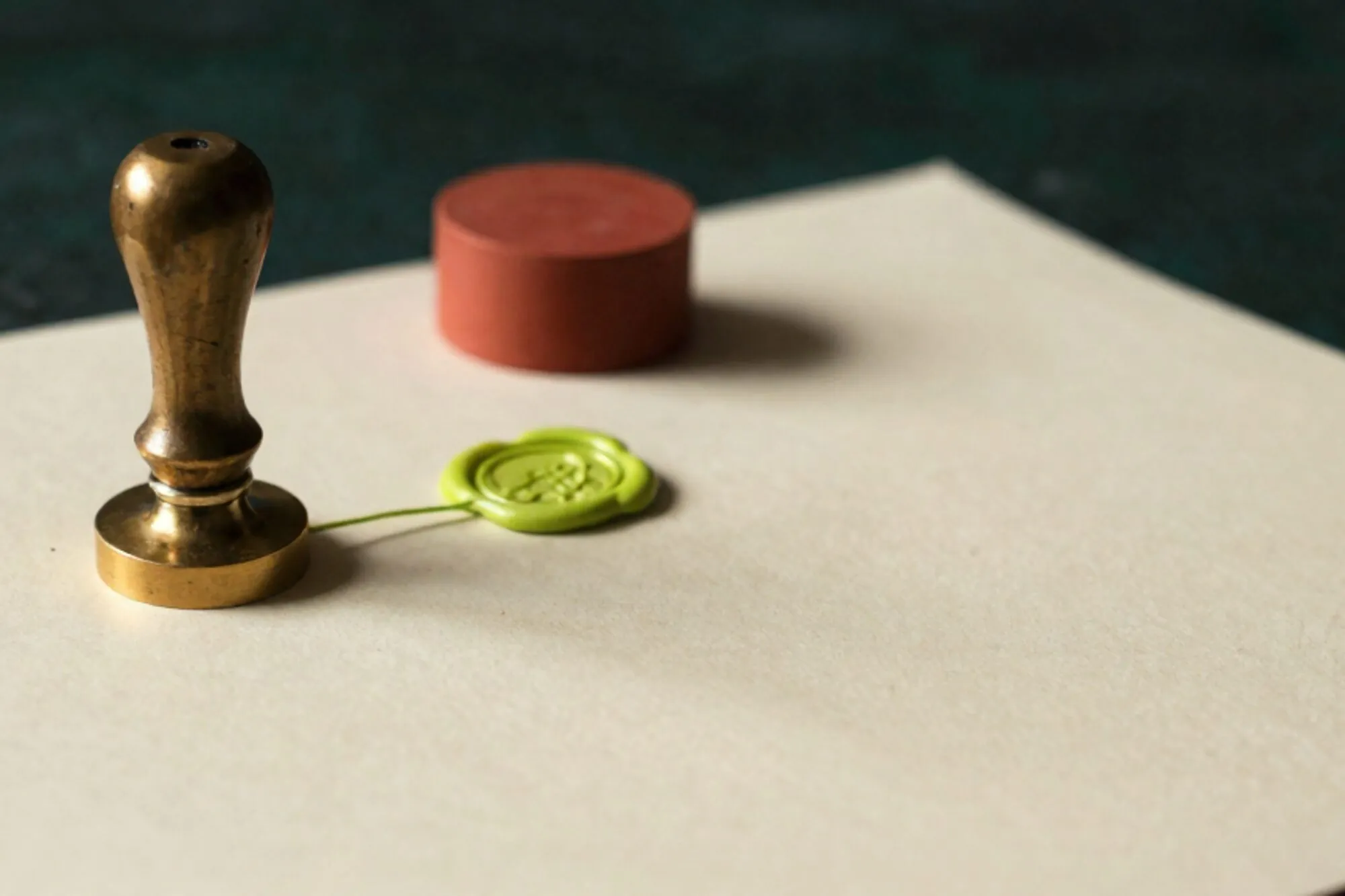 Brass notary seal on cream certificate with duplicate impression, green wax thread, clay-red ink pad, dark green backdrop.