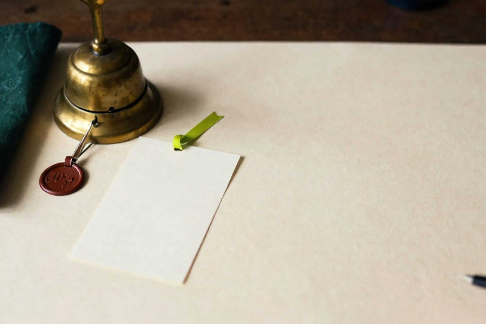 Brass call bell, cream index card with green ribbon, leather collar tag, folded linen cloth on ivory desk.