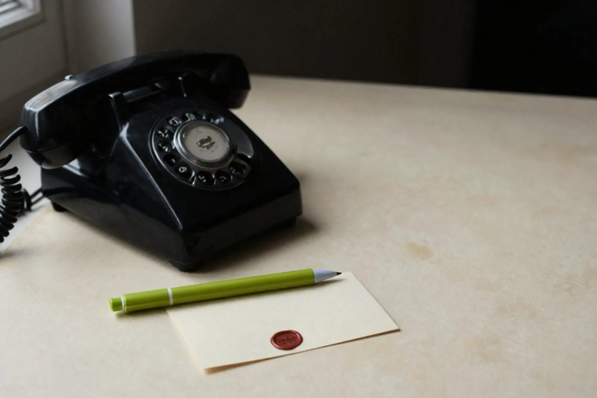 Vintage black bakelite phone receiver off-hook on cream leather blotter, green ribbon, ivory card with red wax seal.