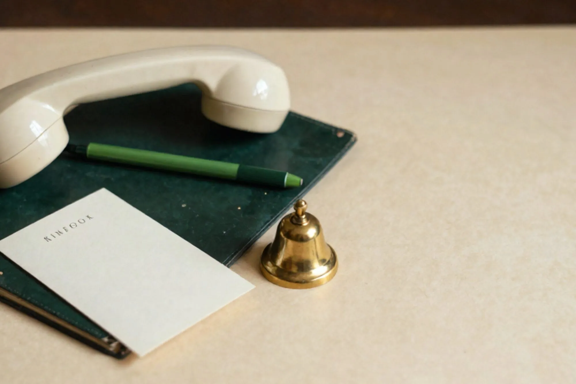 Cream bakelite desk phone on dark green leather blotter, green ribbon on cradle, ivory card, brass bell, red wax seal.