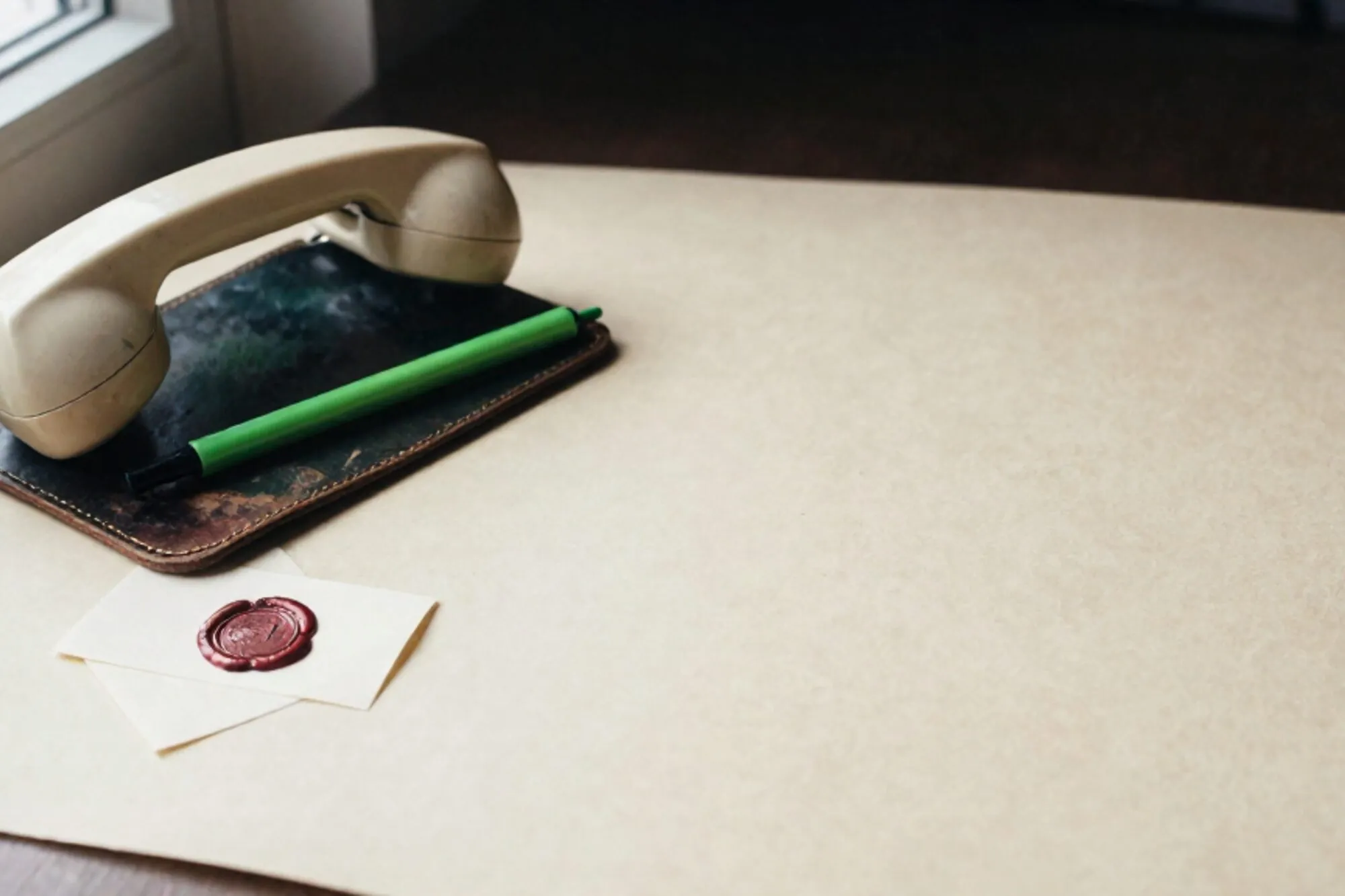 Crème bakelieten telefoonhoorn op donkergroen leren vloeiblad, limoengroen lint, kaartje met rode lakzegel.
