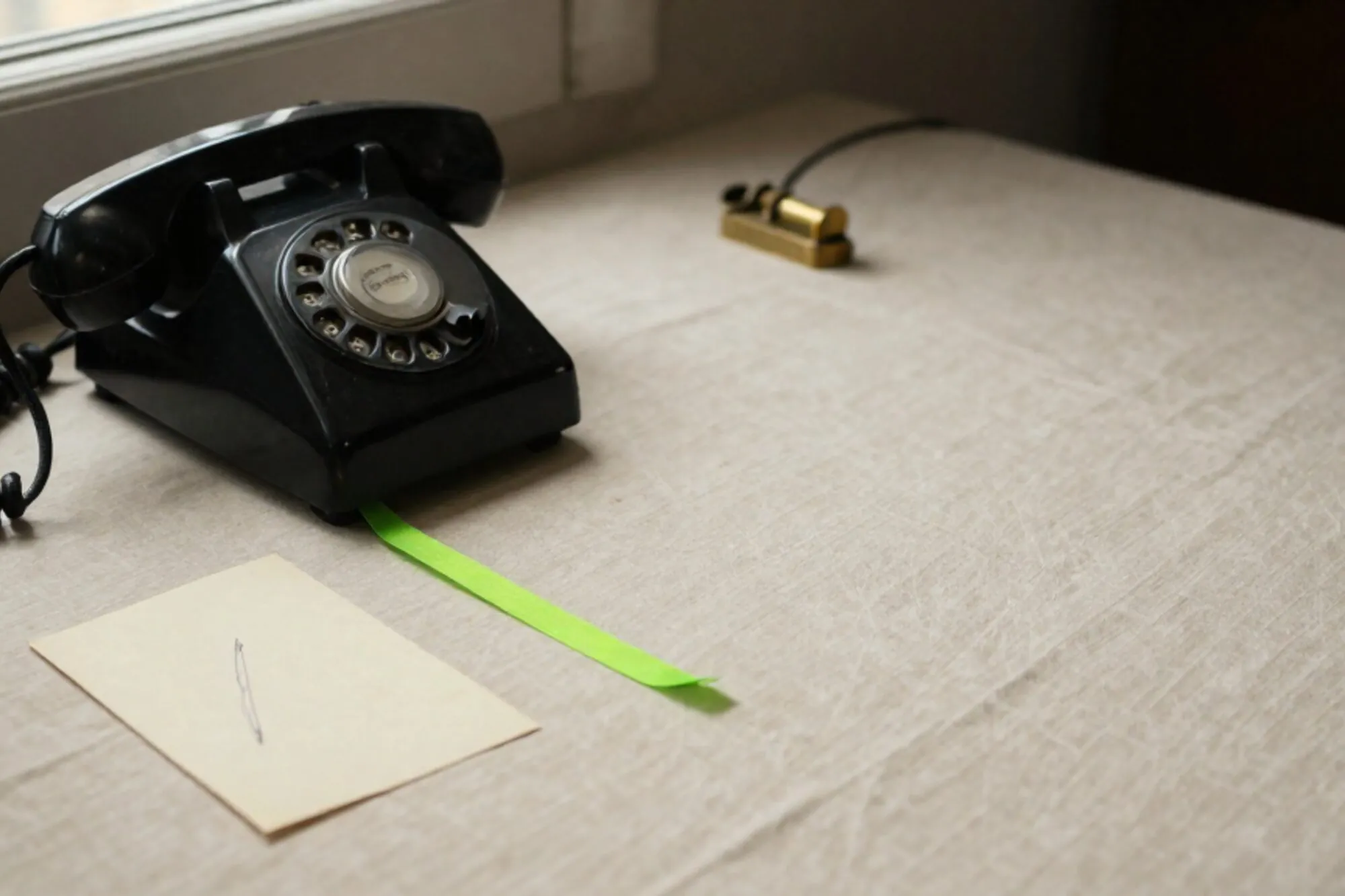 Zwarte bakelieten telefoonhoorn op ivoorkleurig linnen, gekrulde snoer, limoengroen lint, koperen presse-papier, indexkaart.