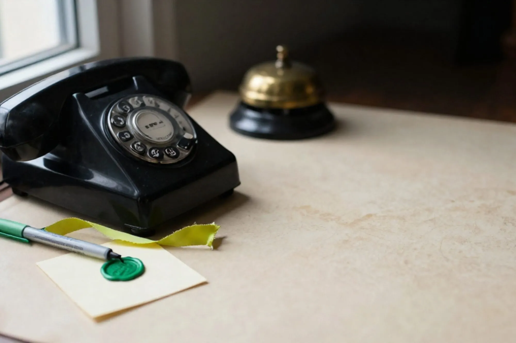 Zwarte bakelieten telefoonhoorn op ivoorkleurig leer, chartreuse lint, kaart met lakzegel, koperen bel op achtergrond.