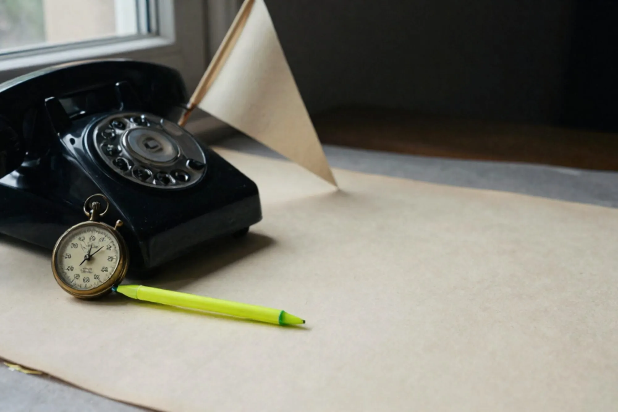 Zwarte bakelieten telefoonhoorn op crème leren onderlegger, koperen stopwatch, groen zijden lint, gevouwen vlag in schaduw.