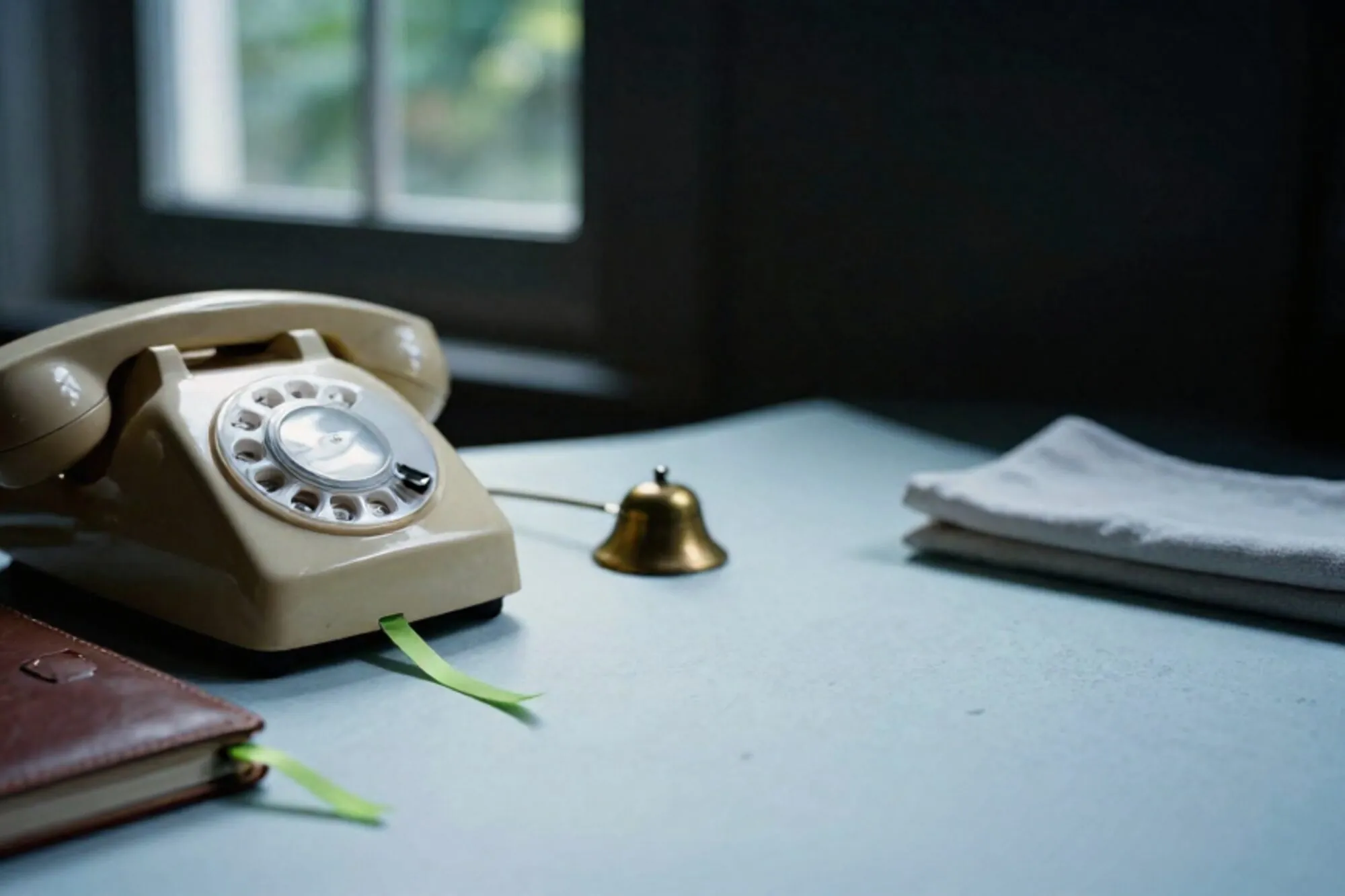 Crème Bakelieten telefoonhoorn op ivoren leren onderlegger, groen lint in agenda, koperen bel, linnen servet.