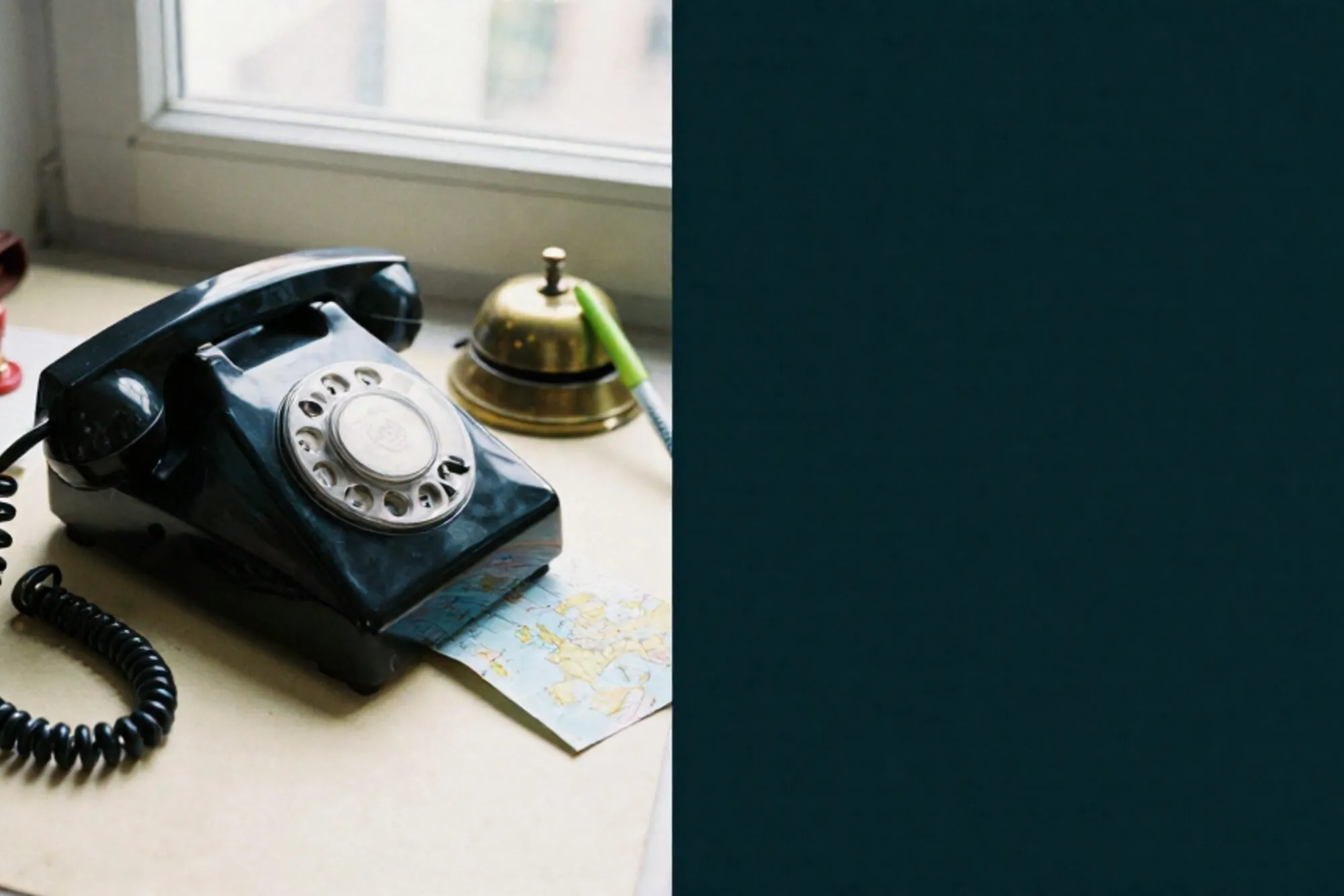Vintage black bakelite phone receiver off-hook on ivory blotter, folded paper map, green ribbon, brass bell, red wax seal.
