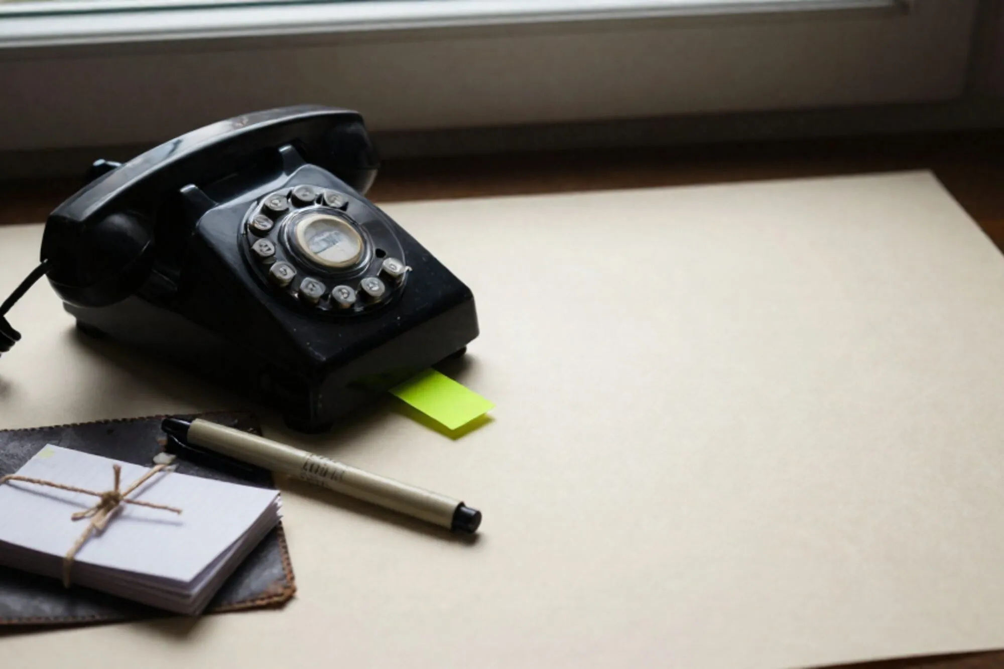 Vintage black bakelite phone off-hook on leather blotter, cream ribbon, green sticky tab, twine-tied job cards.