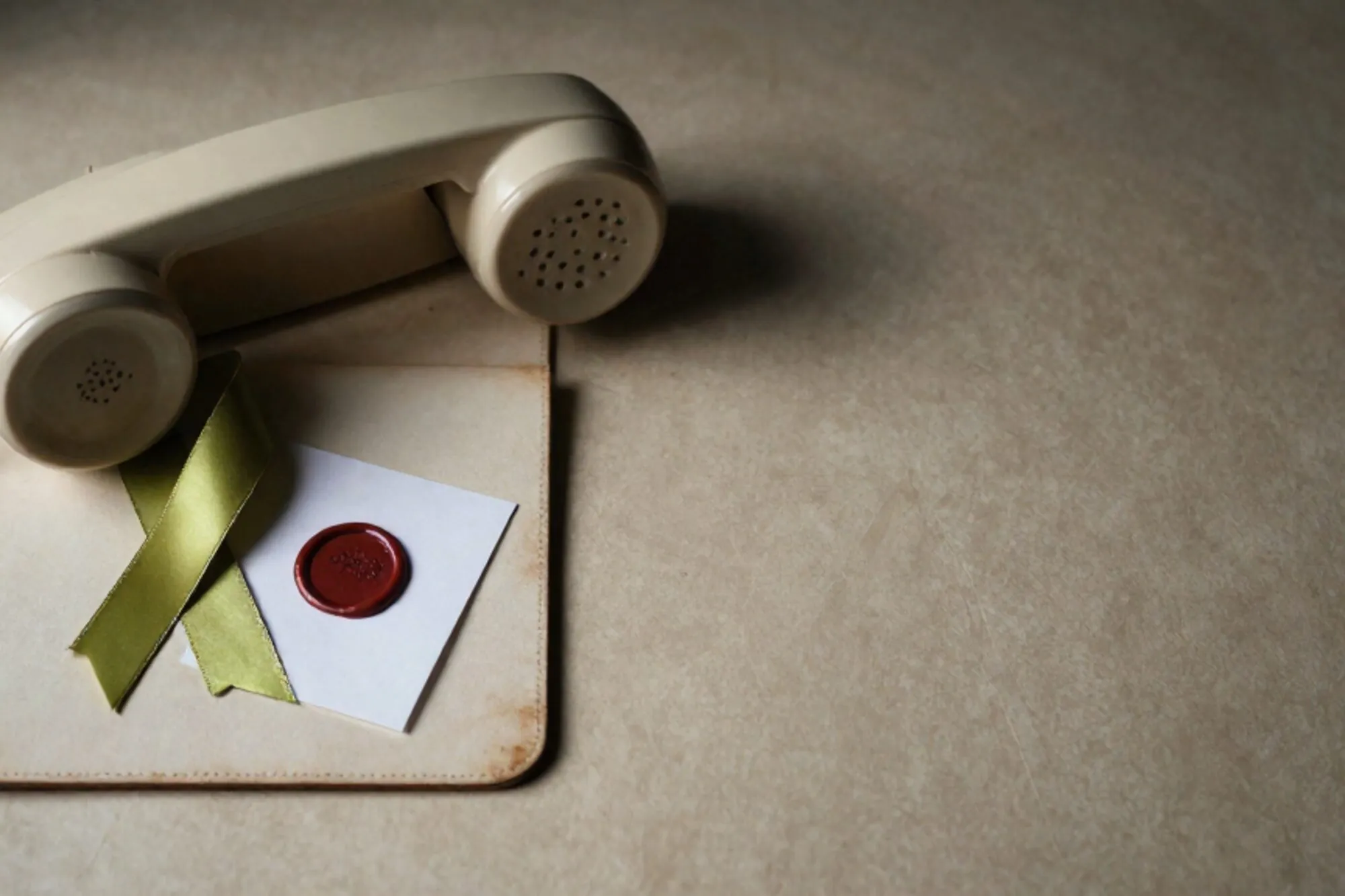 Cream Bakelite phone receiver on ivory leather blotter, green silk ribbon, red wax seal on folded note.
