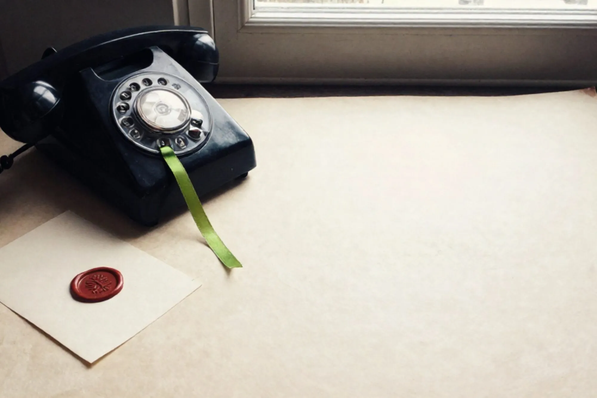 Vintage black bakelite phone receiver off-hook on ivory leather blotter, green ribbon, red wax seal on cream card.