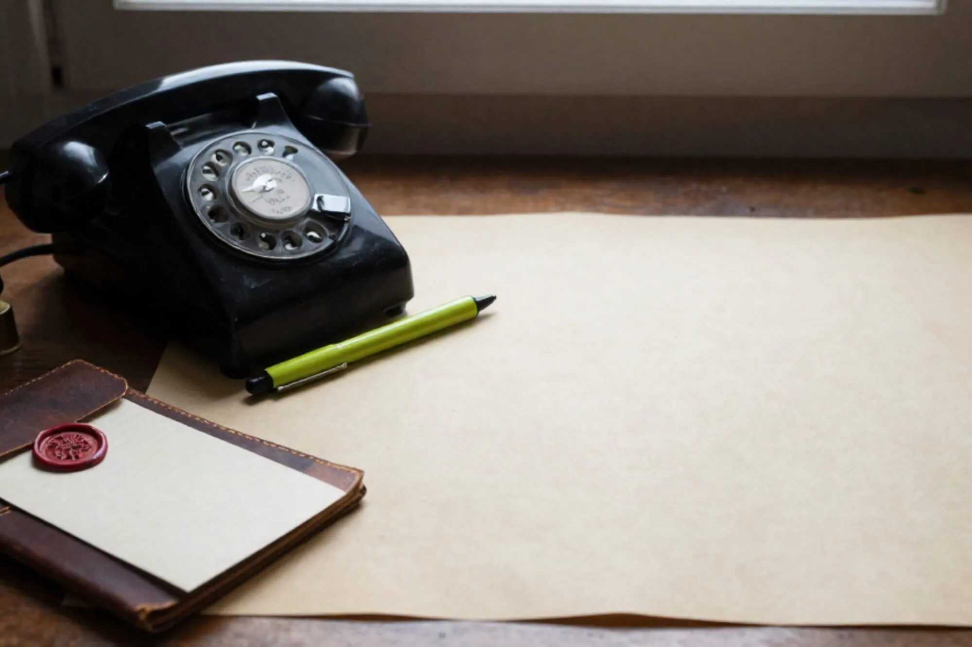 Vintage zwarte bakelieten telefoonhoorn op een mosgroen leren vloeiblad, gekrulde snoer over ivoorkleurig papier.