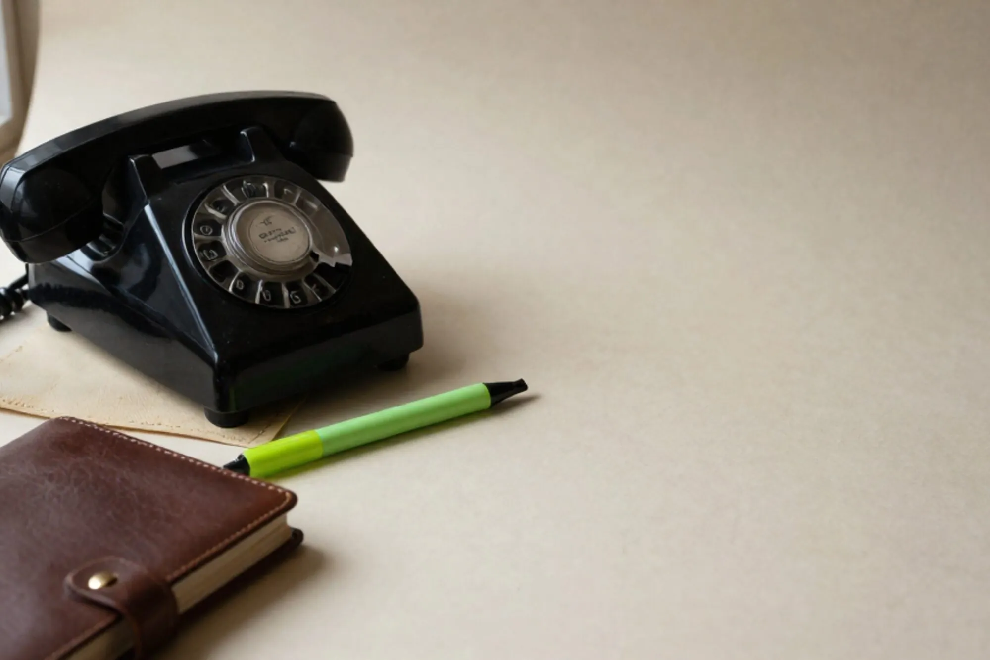 Vintage black bakelite telephone receiver on ivory leather blotter, green silk ribbon trailing from a leather ledger.