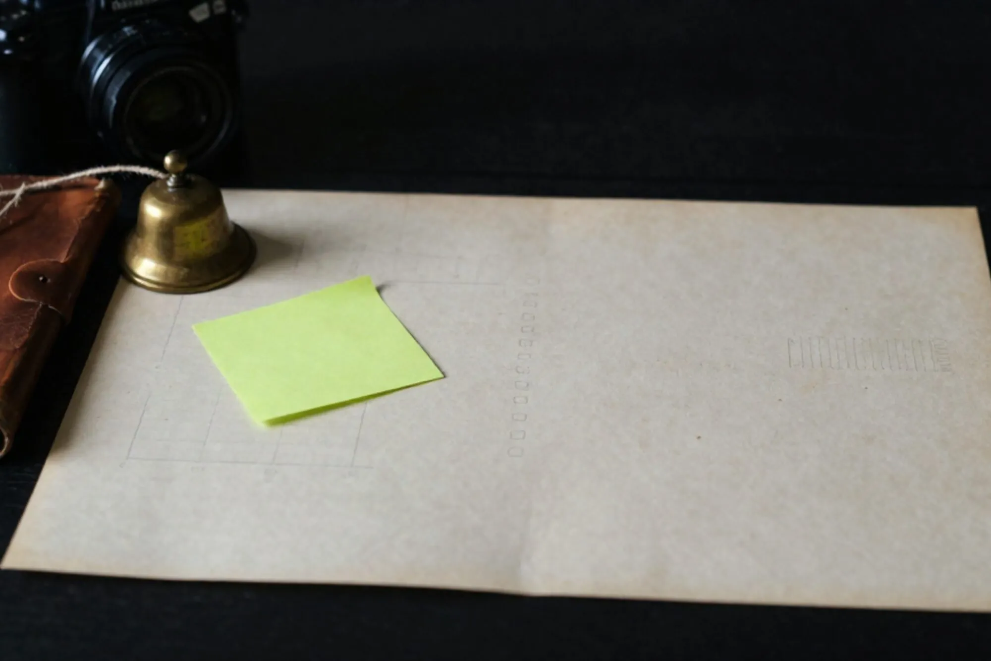 Cream work-order slip with chartreuse sticky note, brass bell, linen twine, leather folio on bone-paper blotter.
