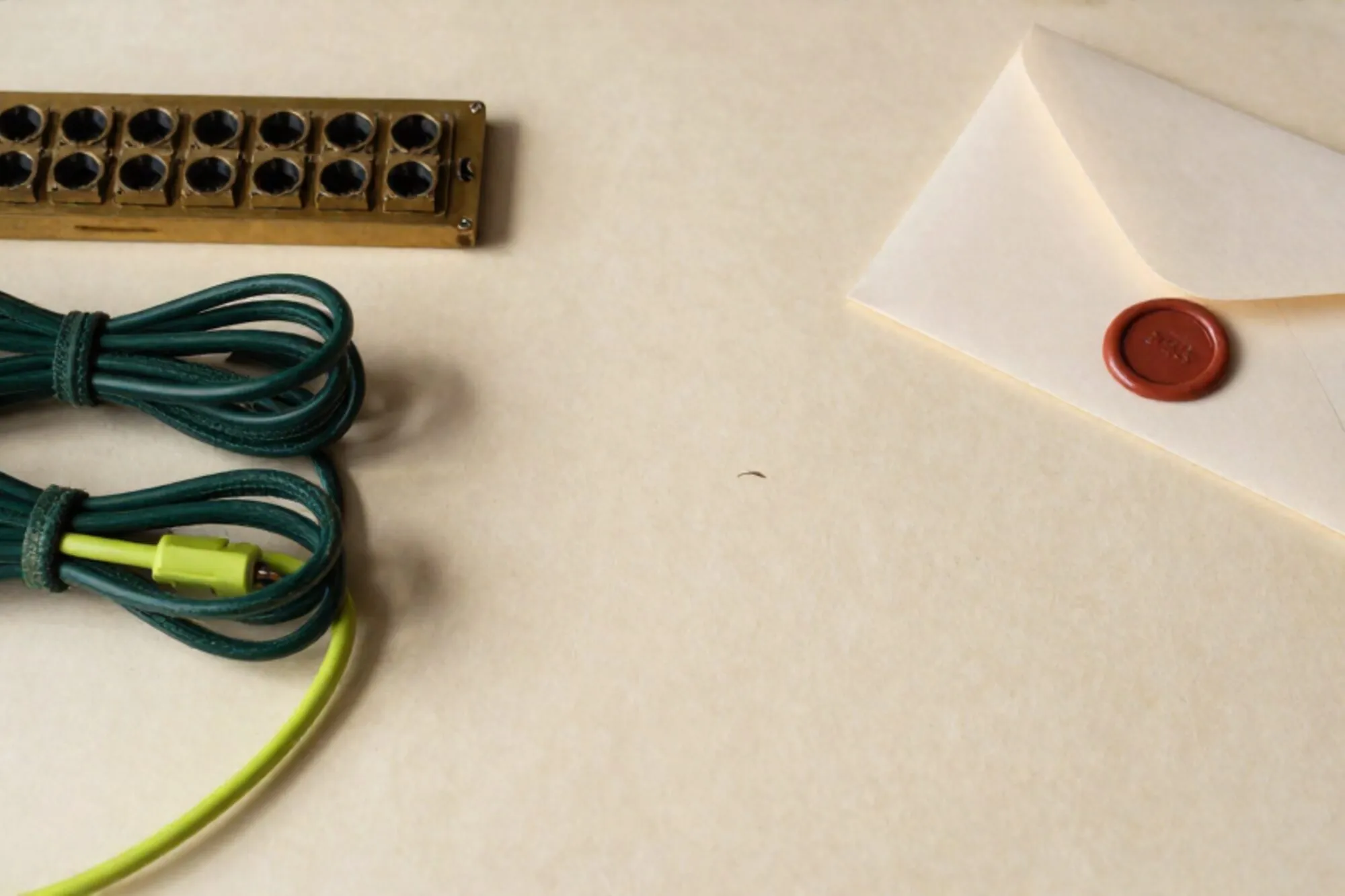 Brass switchboard with eleven green cloth cables coiled, one chartreuse cable trailing, wax seal and envelope on ivory paper.