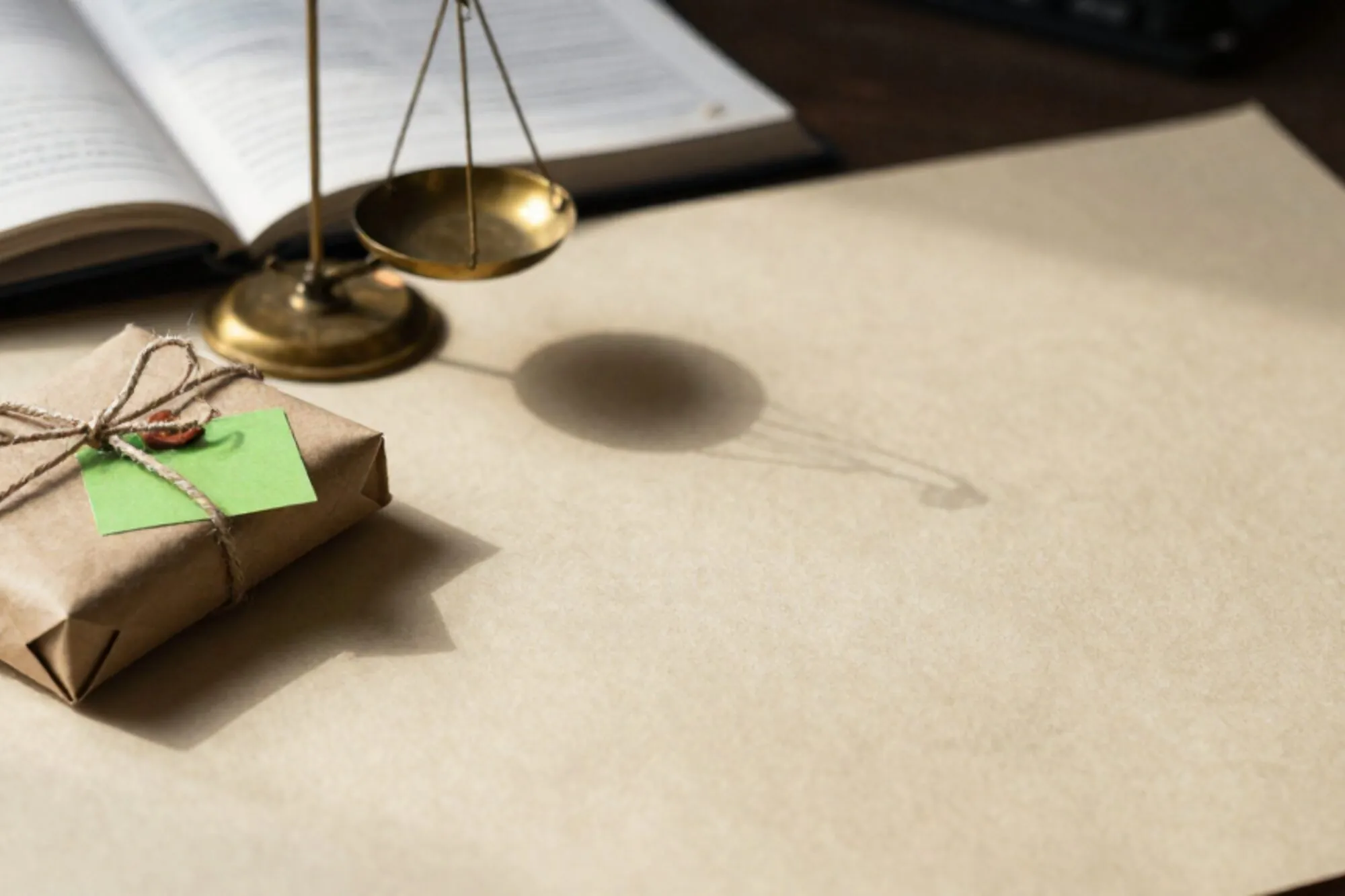 Brown paper parcel tied with linen twine, brass scale, green postcard, open ledger on ivory paper.