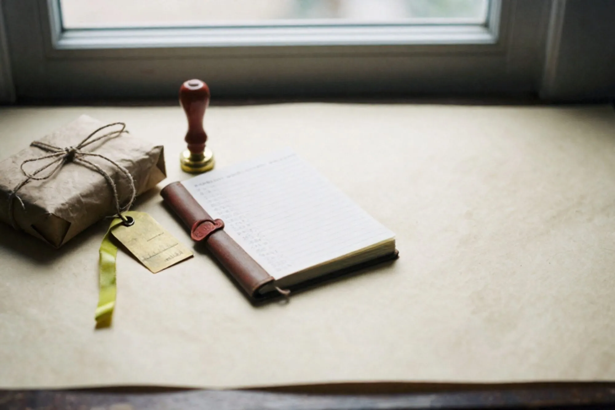 Craft-paper parcel with linen twine, brass tag, leather ledger, green ribbon, red wax seal on ivory paper.