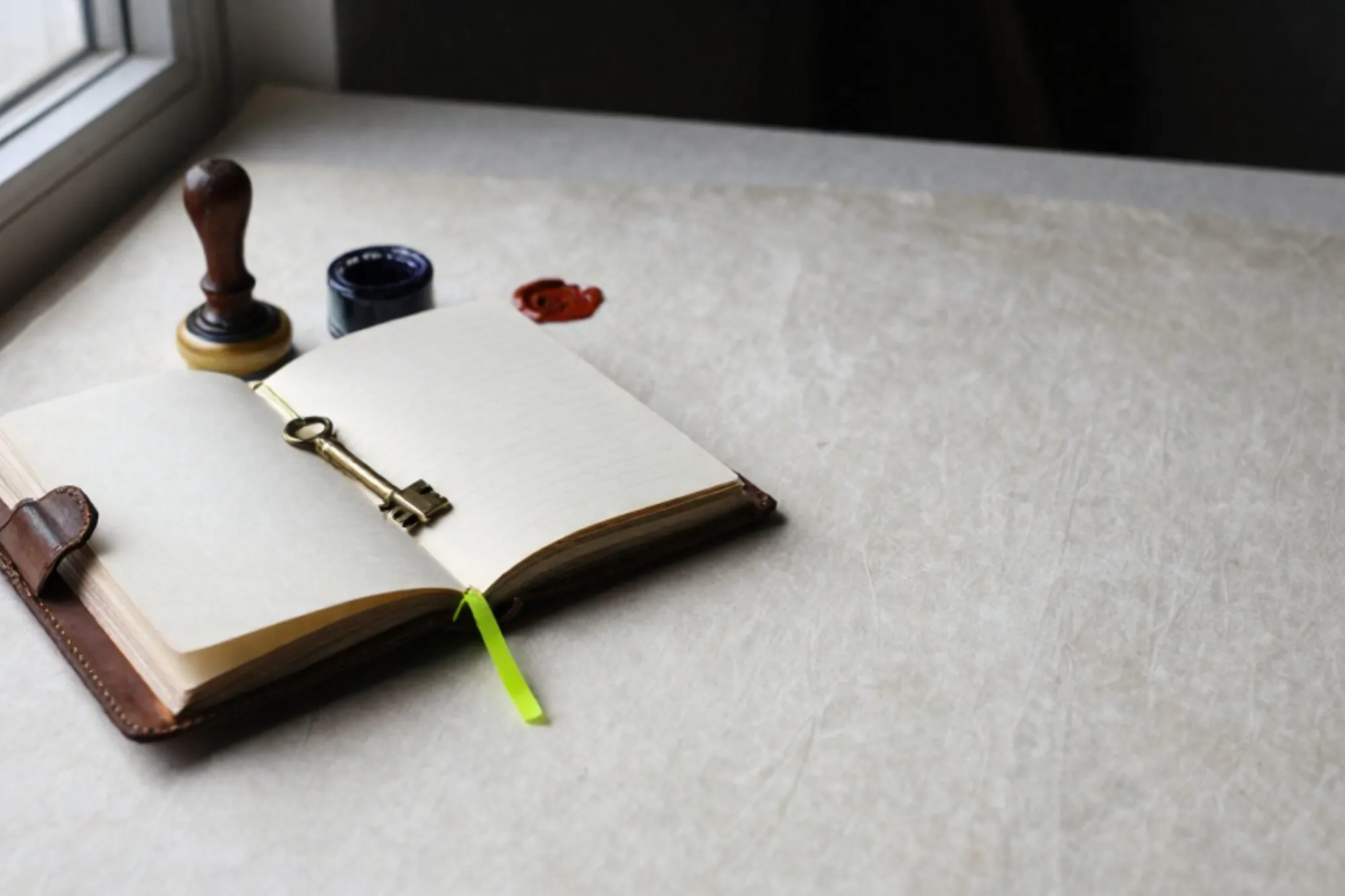 Open leren logboek met messing sleutel op crème kaart, inktkussen, stempel, groen lint, lakzegel op ivoren linnen bureau.