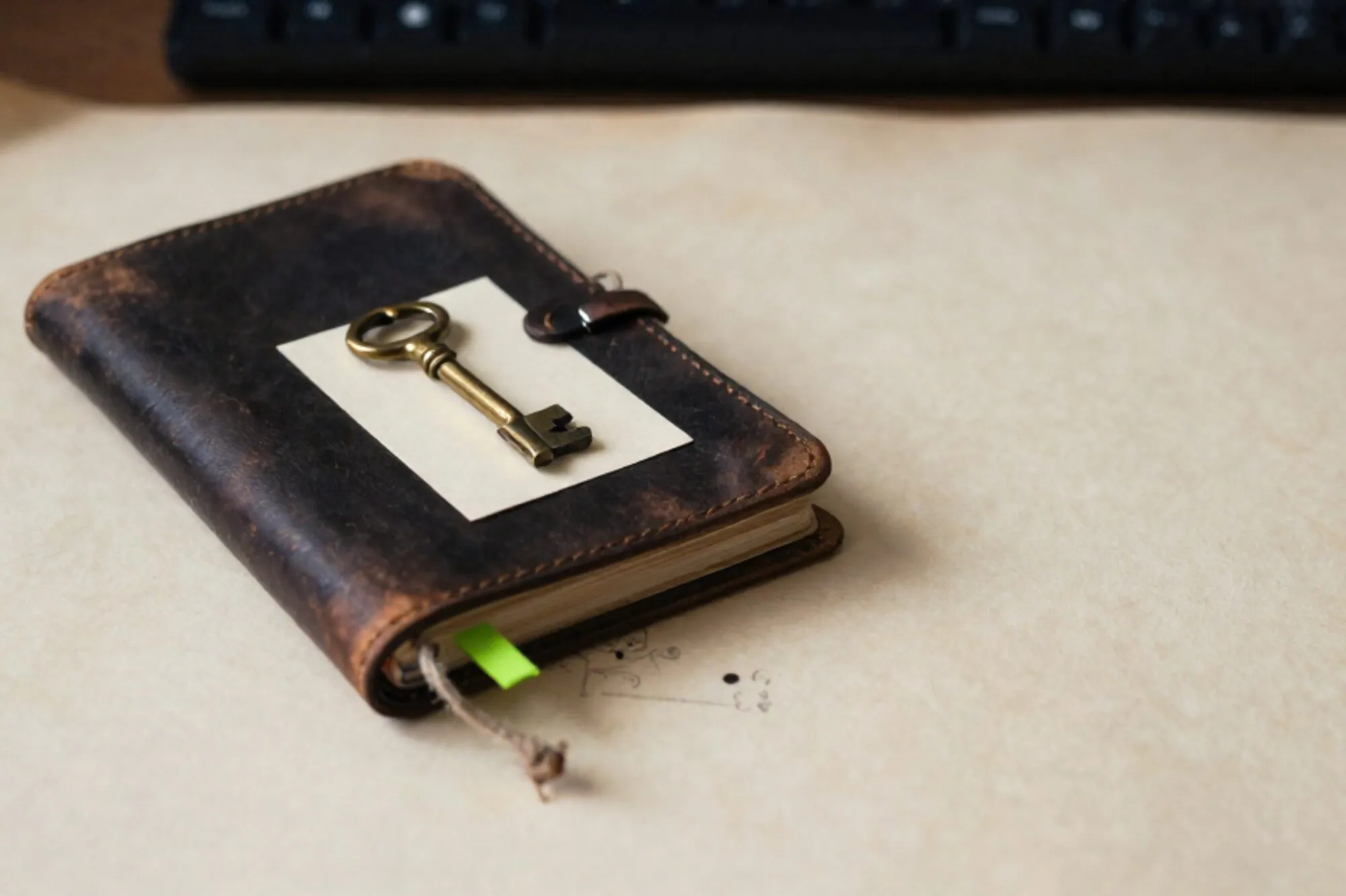 Gesloten leren logboek met linnen koord, koperen sleutel op crème kaartje, groen lint, op ivoorkleurig papier.