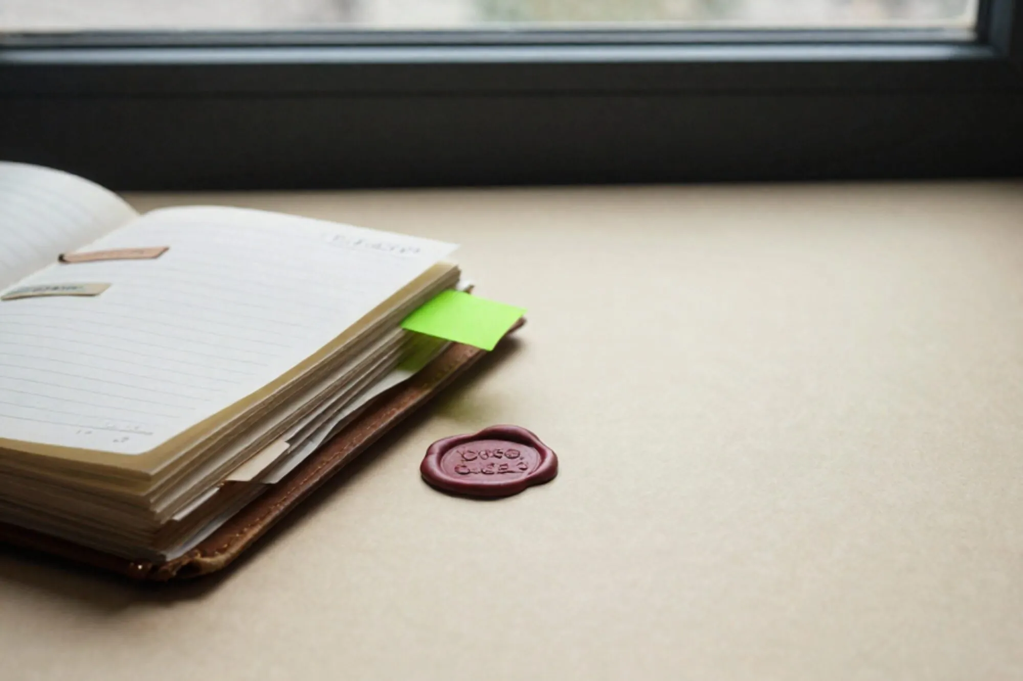 Open versleten leren logboek met overvolle papieren tabs, een groen label en rood lakzegel op ivoorpapier.