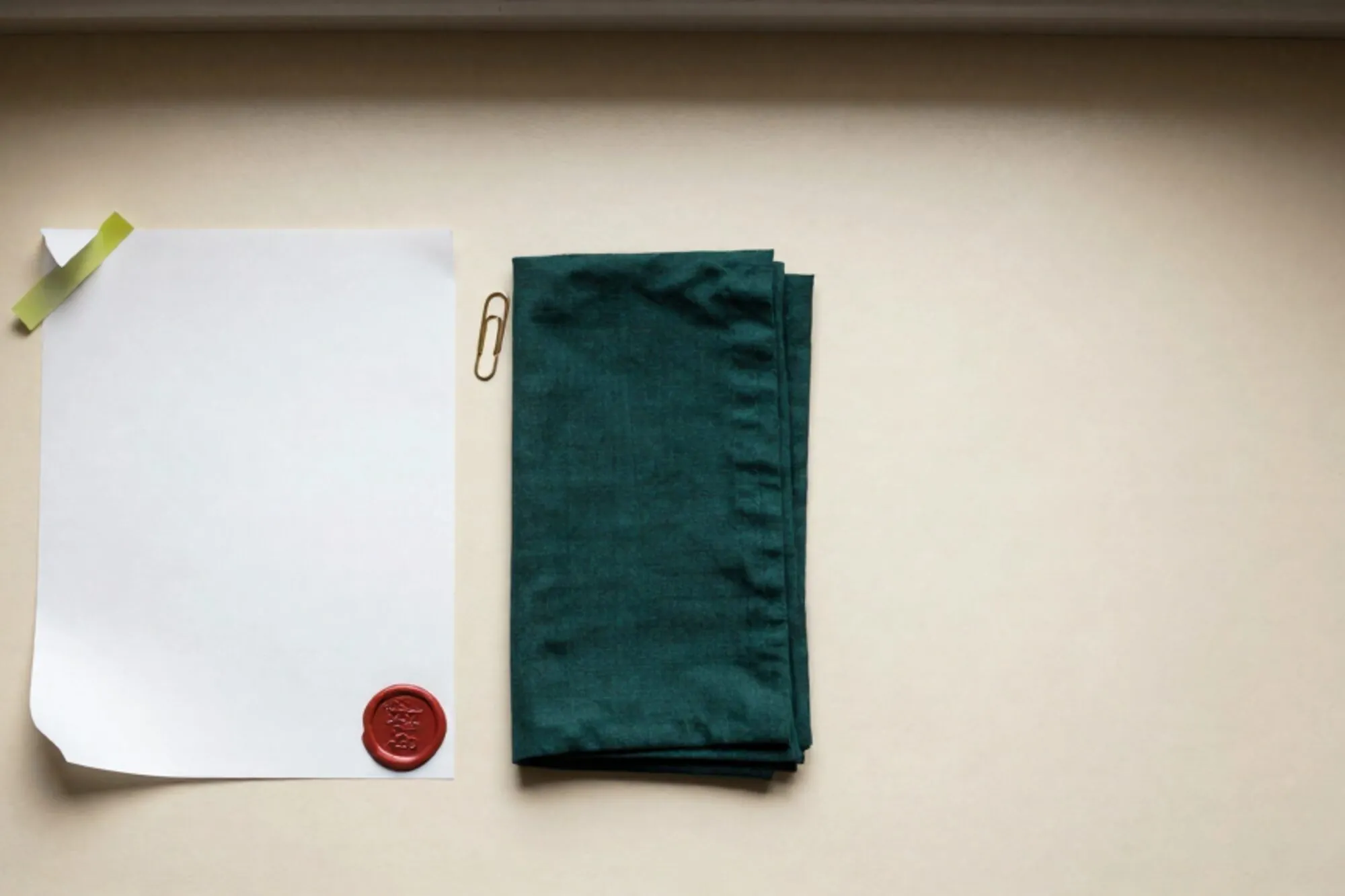 Printed letter with curled corner on ivory desk, green sticky tab, brass paper clip, linen napkin, red wax seal.