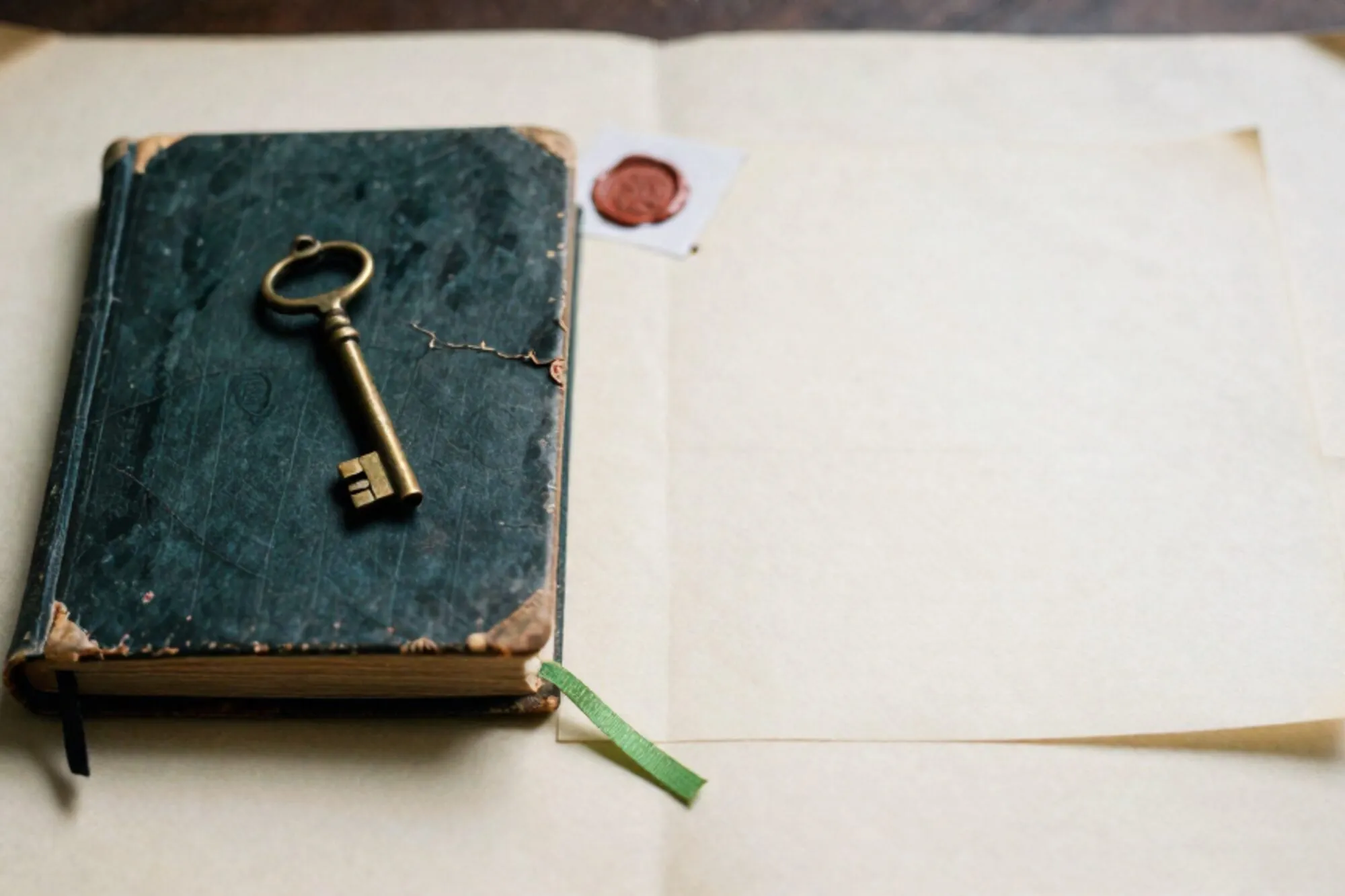 Versleten linnen handboek met messing sleutel, calqueerpapier, groen lintje en rood lakzegel op ivoorkleurig vlak.