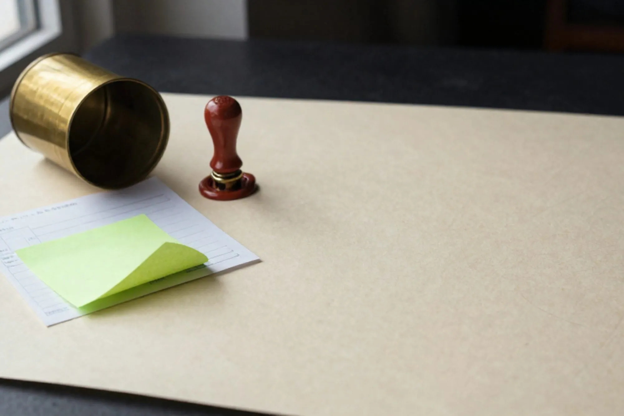 Open koperen buispostkoker naast gevouwen factuur, groene memo, gebroken rood wax-zegel op ivoren bureau.